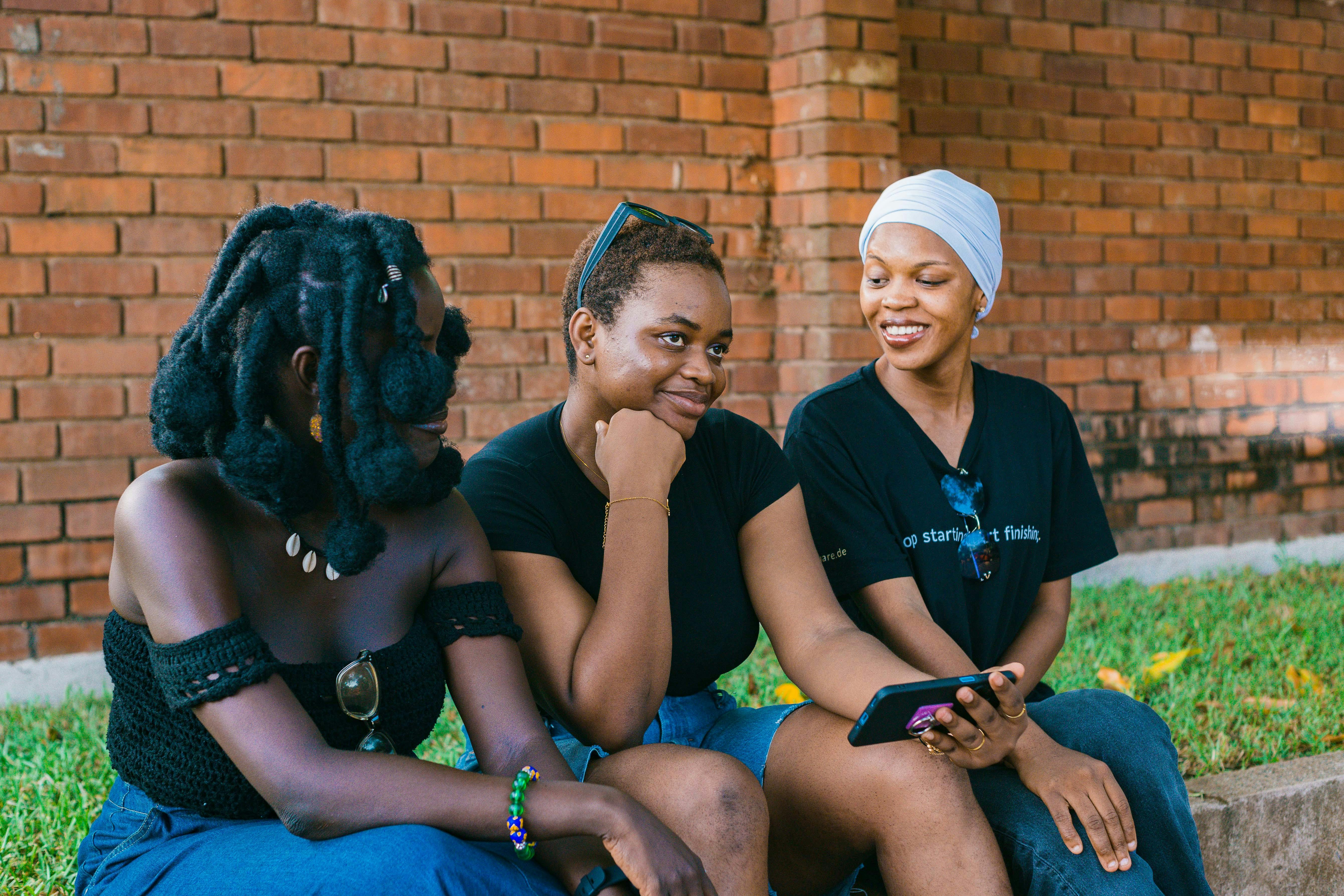 ฟรี หญิงสาวสามคนกำลังสนทนากันอย่างสบายๆ กลางแจ้งข้างกำแพงอิฐในเมืองอักกรา ประเทศกานา คลังภาพถ่าย