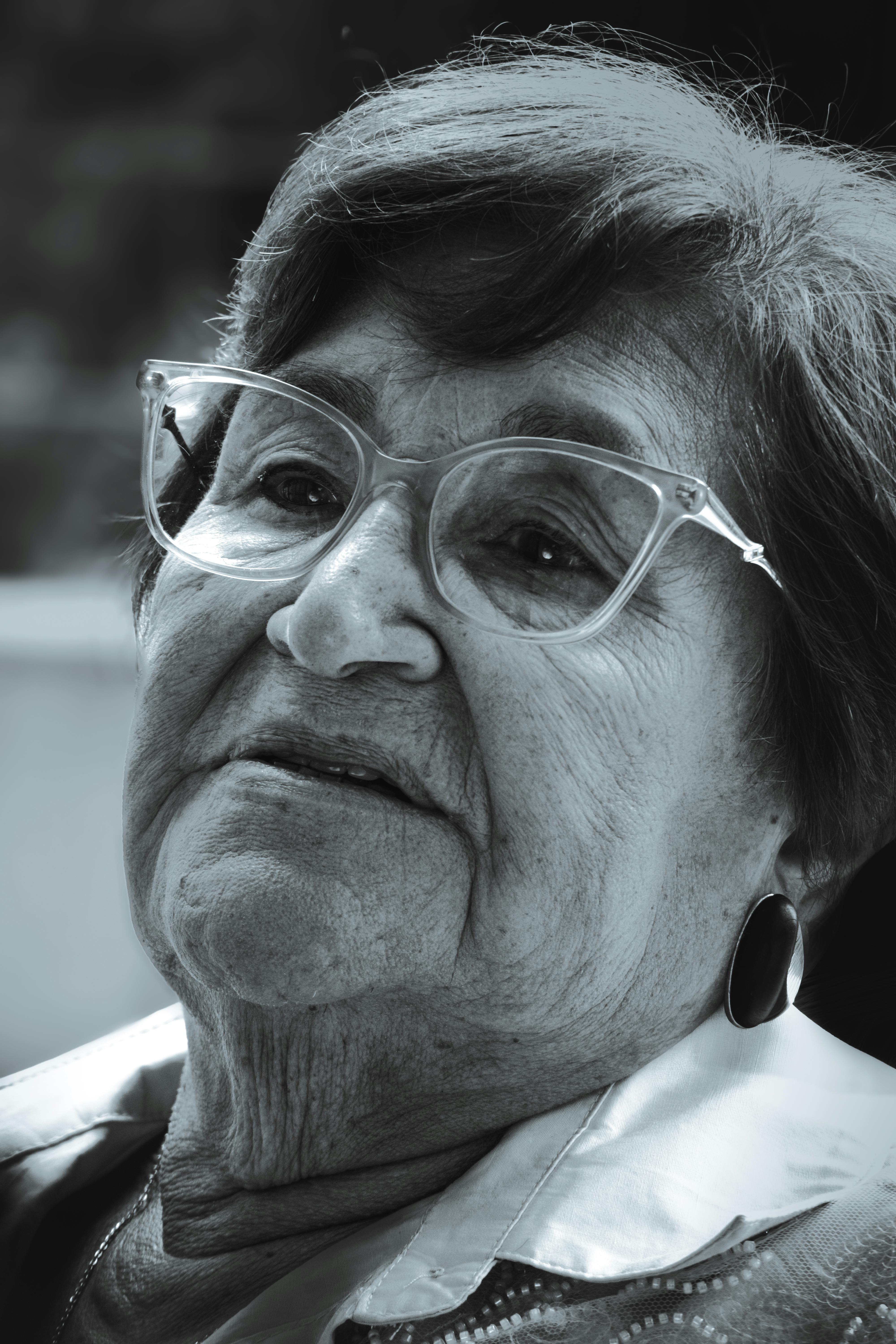 Black and white close-up portrait of an elderly woman wearing glasses, exuding wisdom and warmth.