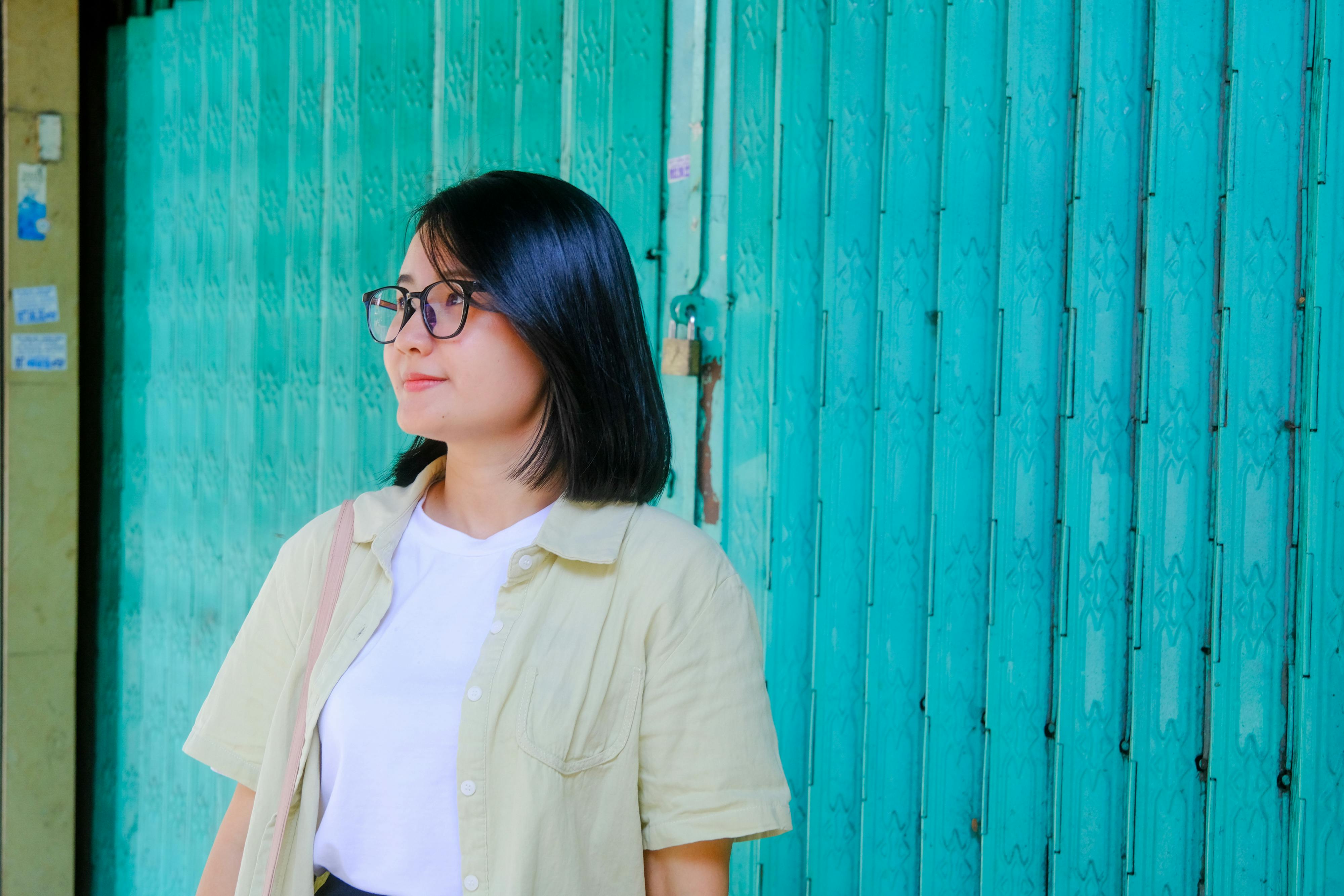 ingyenes Egy stílusos szemüveges nő áll egy türkizkék fémajtó előtt Ho Si Minh-városban. Stockfotó