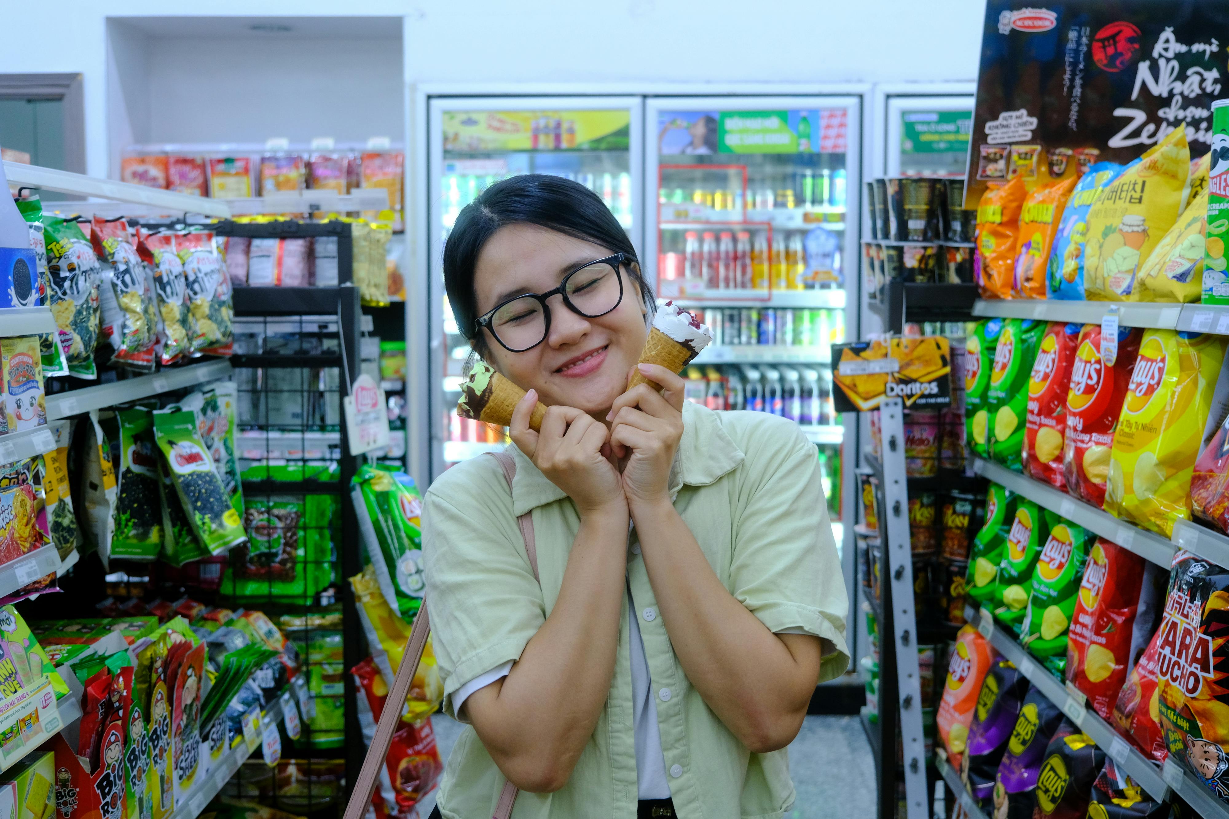 ingyenes Fiatal nő fagylaltot fogyaszt színes falatkák között egy Ho Si Minh-városi üzletben. Stockfotó