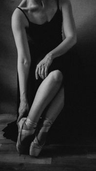 A graceful ballerina adjusts her pointe shoes in an artistic black and white composition.