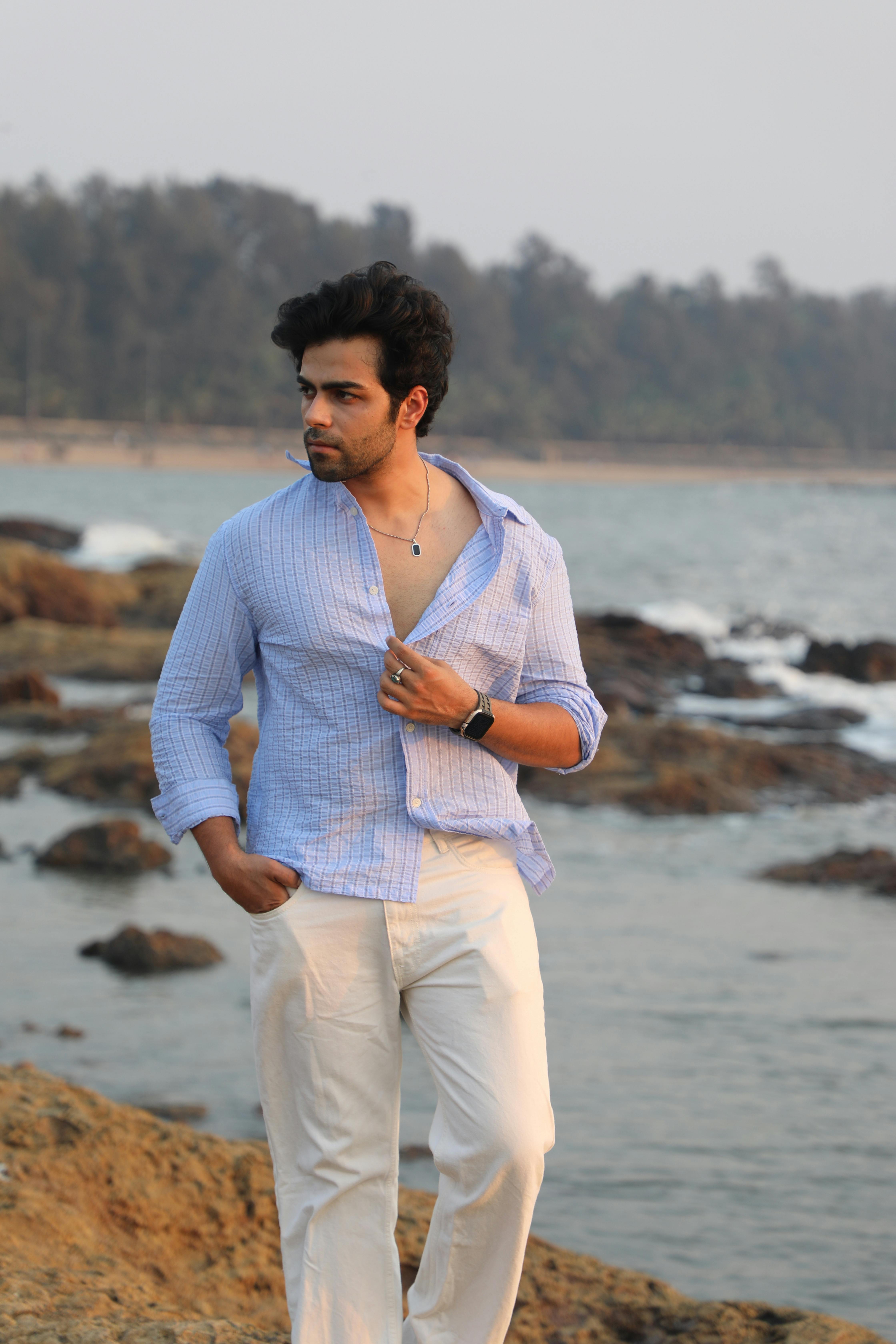 Young man in casual attire walking along a rocky coastline during sunset, reflecting a relaxed vibe.
