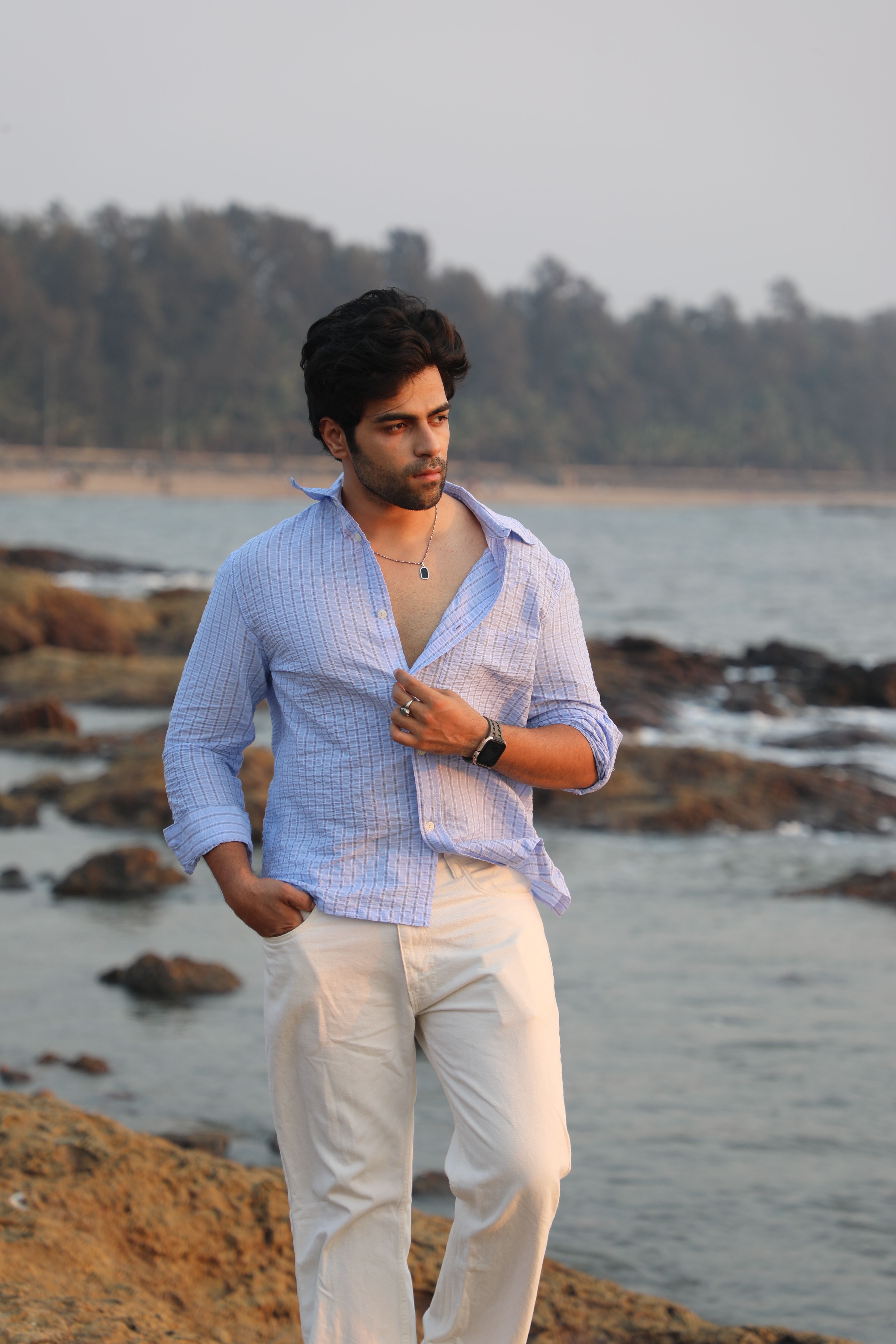 Portrait of a man walking by the sea at sunset, wearing a casual outfit.