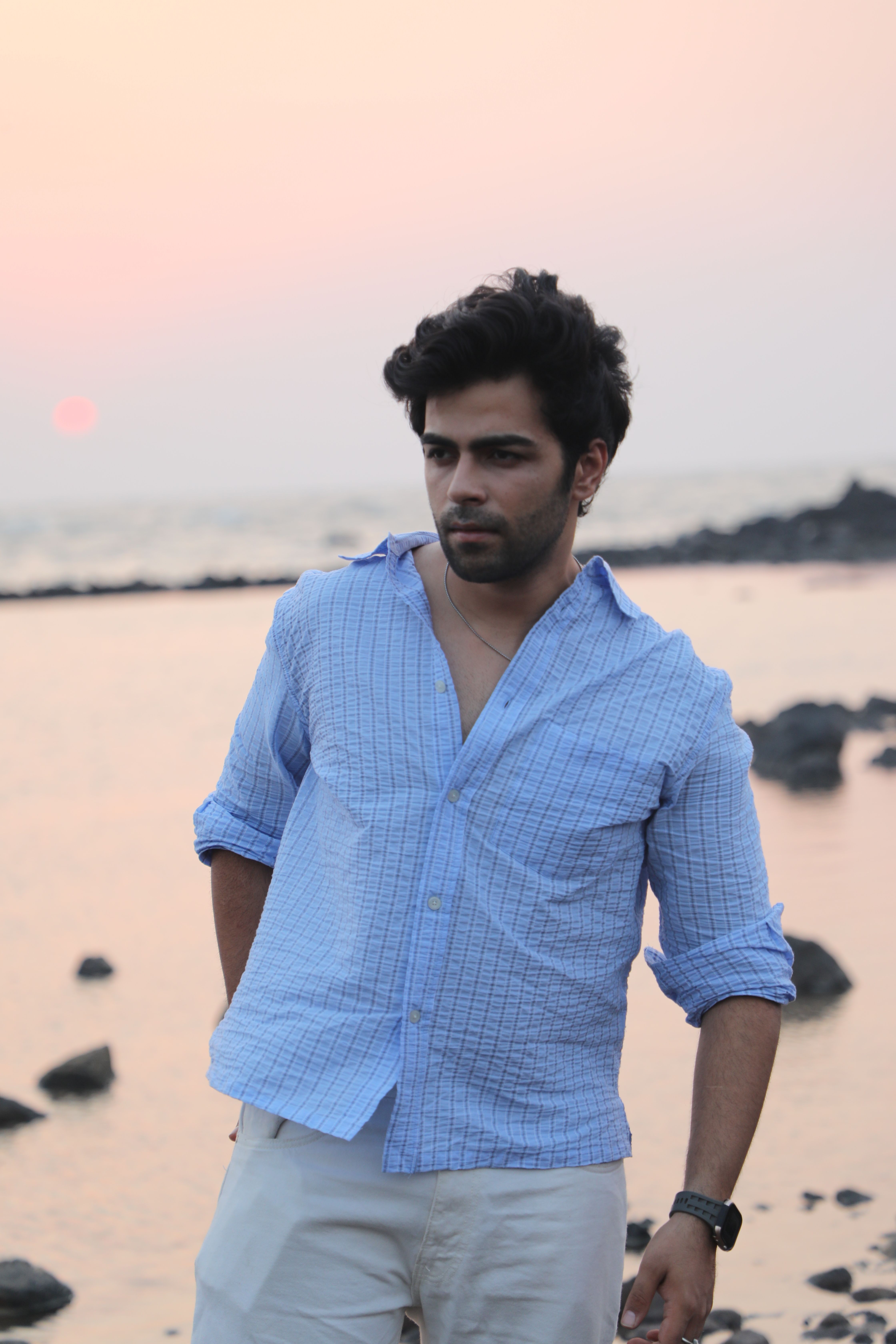 Casually dressed man at sunset on a rocky beach, exuding a relaxed vibe.
