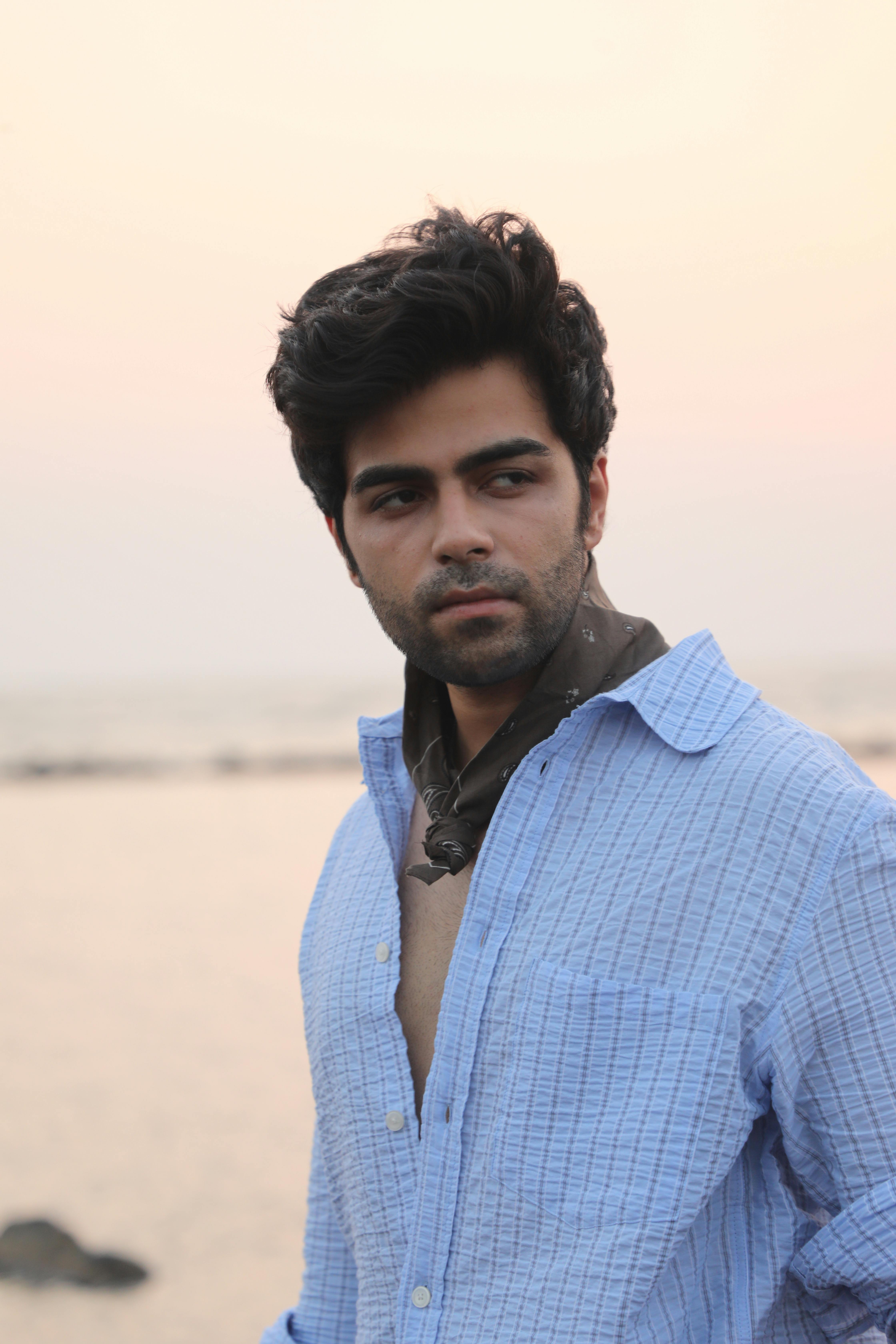 A contemplative man in a blue shirt stands by the beach during a serene sunset.