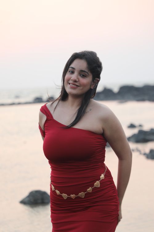 Free Smiling woman in a red dress posing on a rocky beach during sunset. Stock Photo