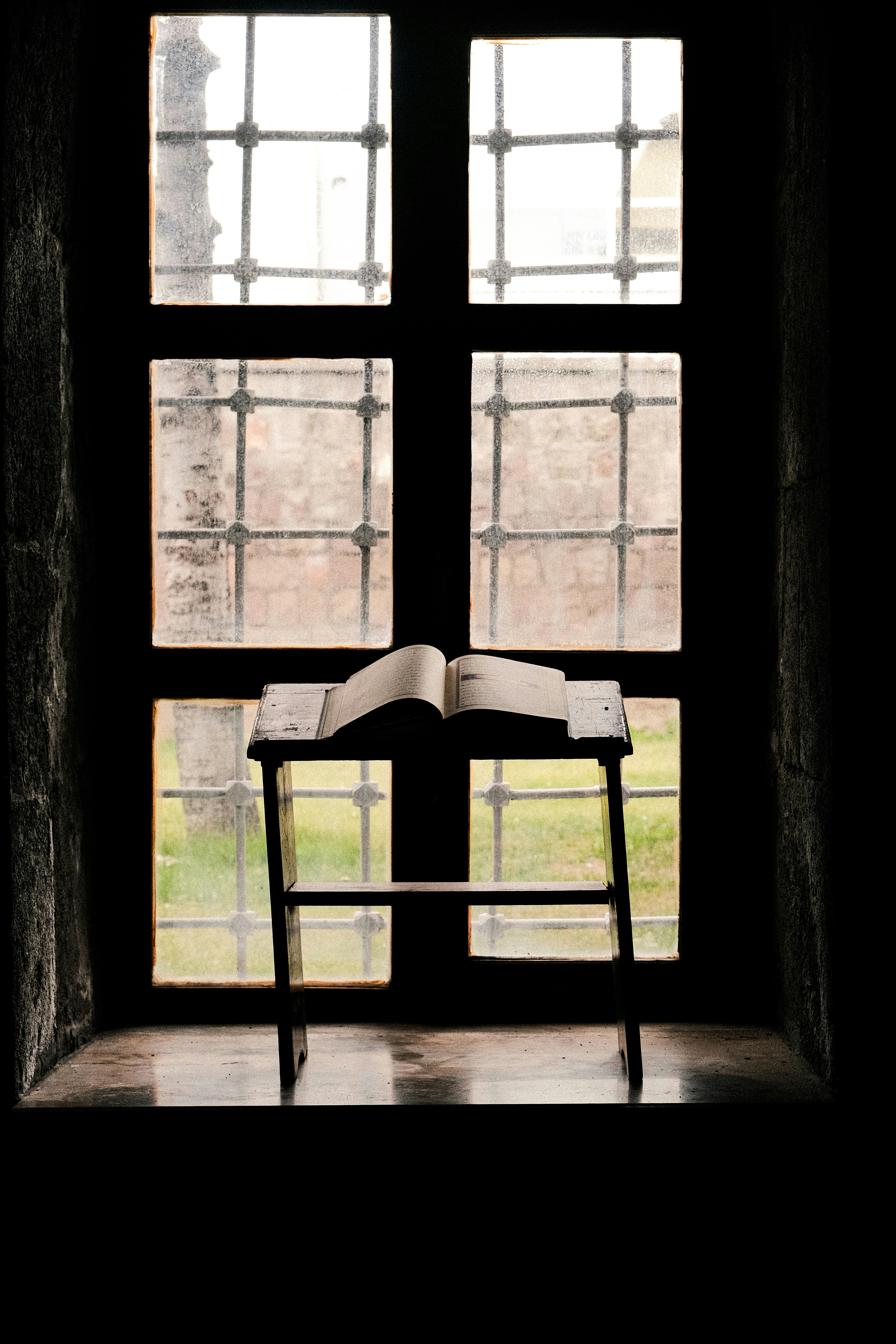 ฟรี หนังสือเปิดเล่มสไตล์ชนบทวางอยู่บนแท่นไม้หน้าหน้าต่างวินเทจ สร้างบรรยากาศที่สงบและให้ความรู้ คลังภาพถ่าย