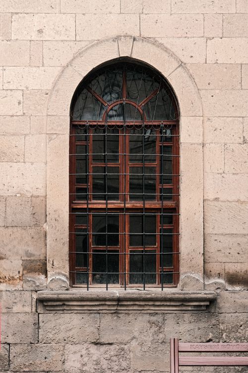 Free A vintage arched window with iron grills set in a stone wall, offering a classic architectural look. Stock Photo