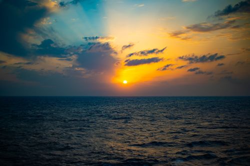 Free A breathtaking sunset over the ocean with vibrant colors illuminating the sky and clouds. Stock Photo