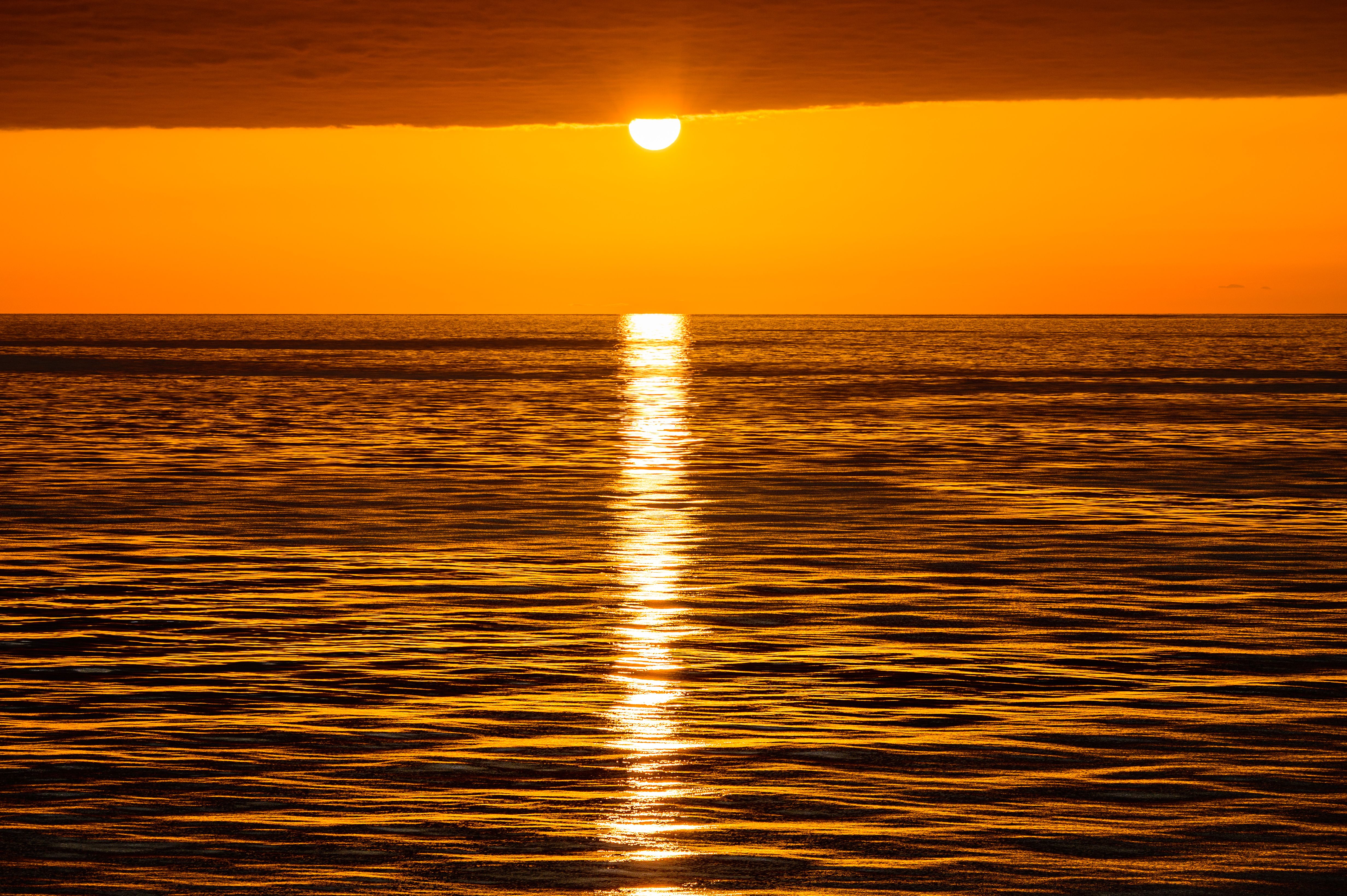 Stunning golden sunset reflecting over calm ocean waters, creating a serene and warm atmosphere.