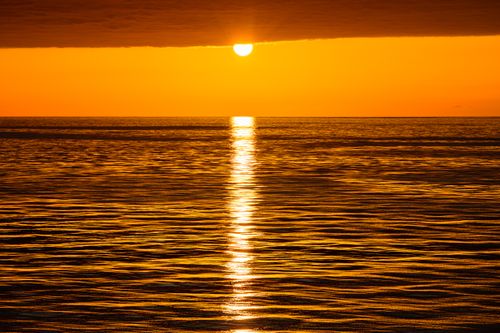 Free Stunning golden sunset reflecting over calm ocean waters, creating a serene and warm atmosphere. Stock Photo