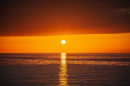 Breathtaking view of a bright orange sunset casting reflections on a calm ocean surface.