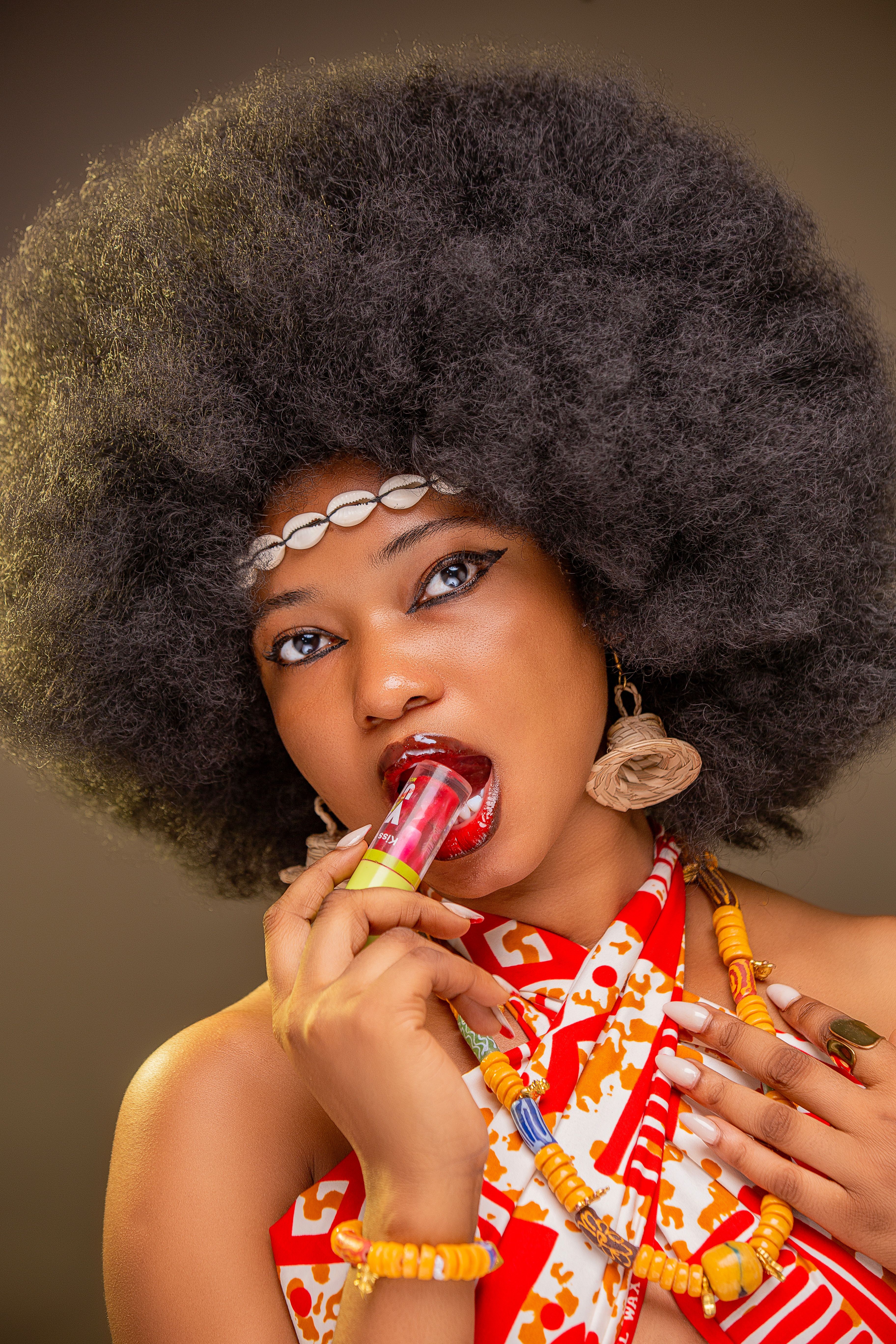 Vibrant portrait of a woman in traditional wear and Afro hairstyle holding lipstick.