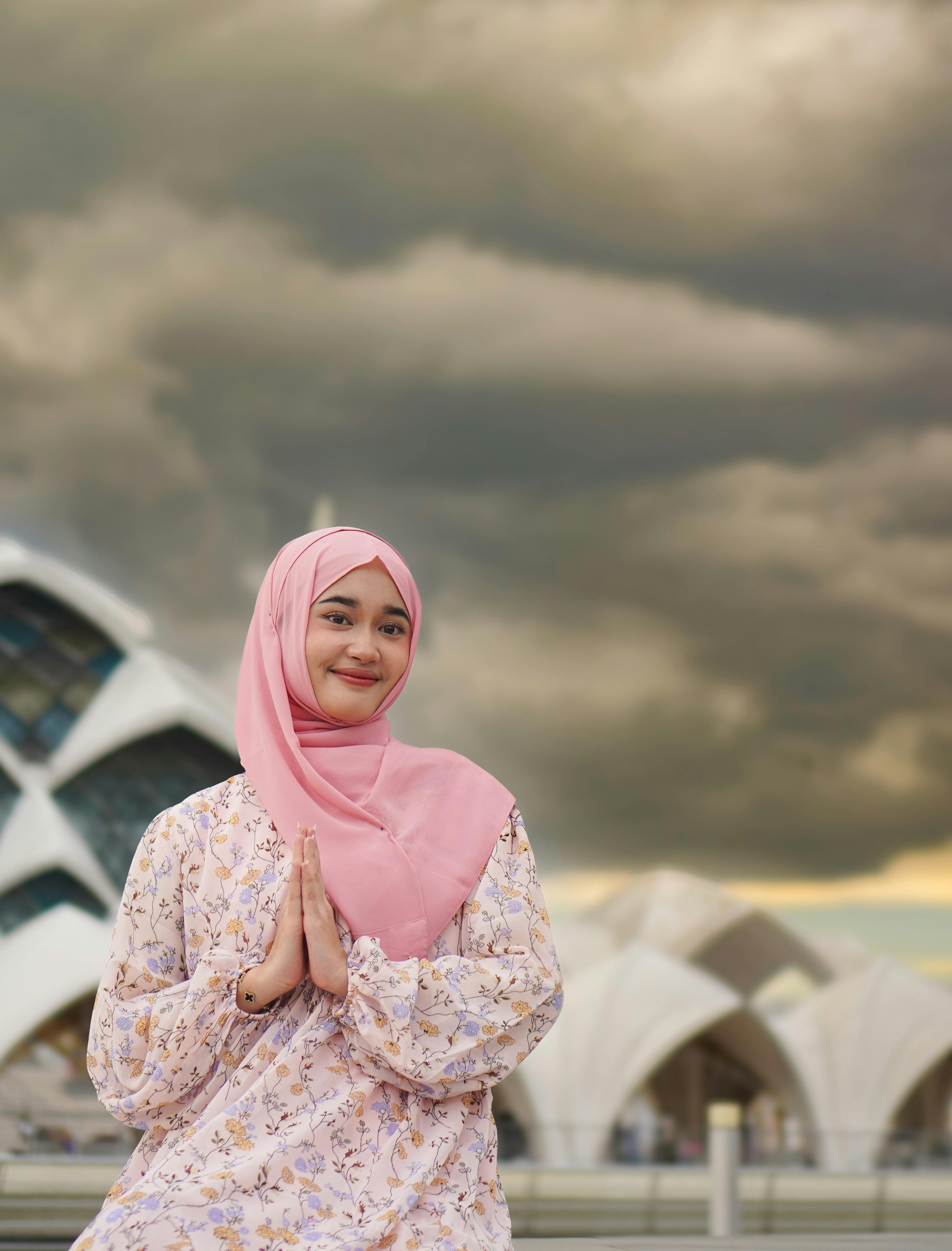 ฟรี หญิงสาวสวมฮิญาบสีชมพูโพสท่าด้วยท่าทางสงบนิ่งท่ามกลางท้องฟ้าที่สวยงามตระการตา คลังภาพถ่าย