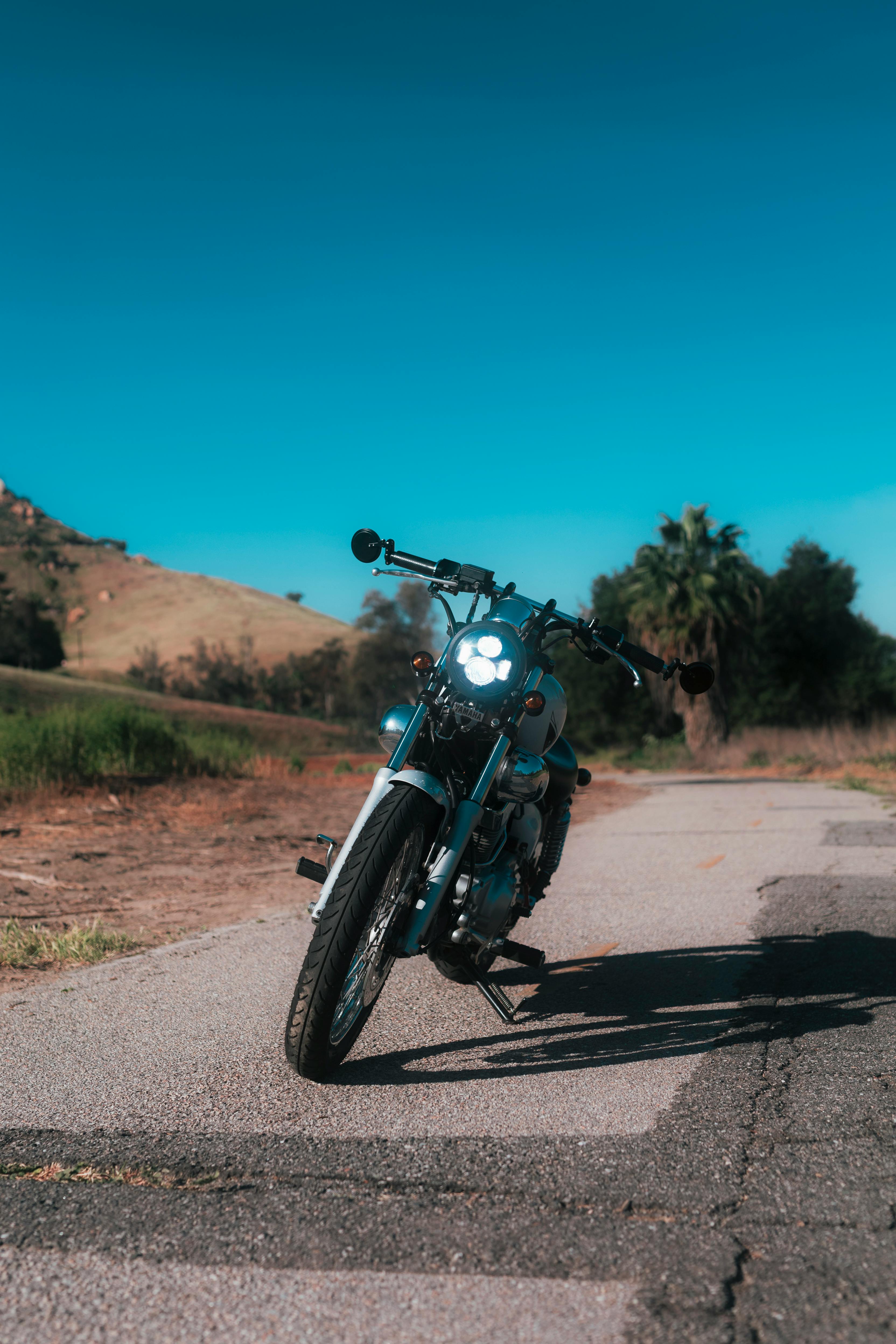 ฟรี รถจักรยานยนต์โบราณจอดอยู่ริมถนนชนบทที่แดดส่องถึง โดยมีเนินเขาสวยงามเป็นฉากหลัง คลังภาพถ่าย