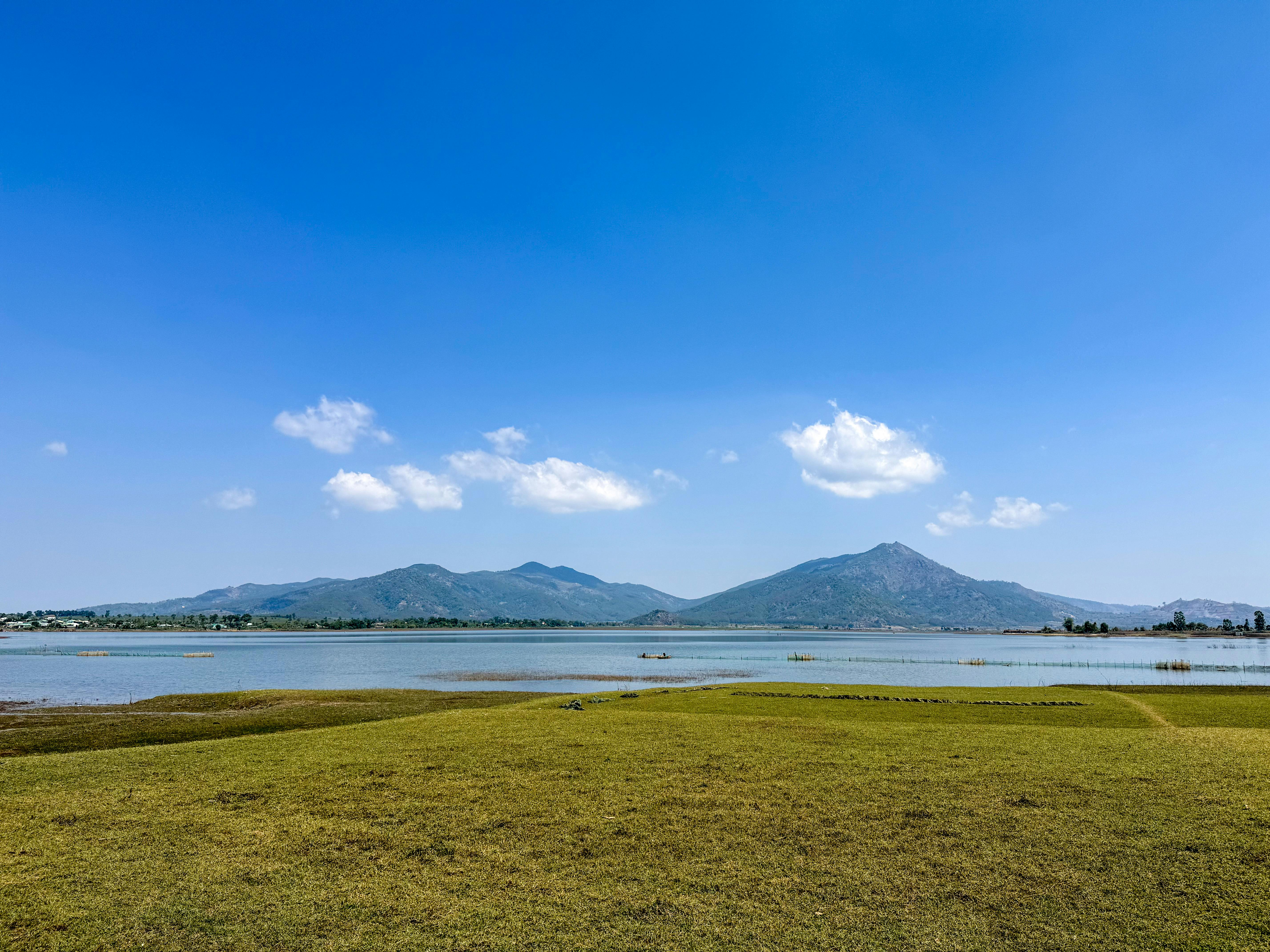 A serene view of Pleiku's lake with distant mountains under a clear blue sky.