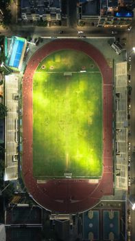 A top-down nighttime shot of a brightly lit athletic stadium with a track field.