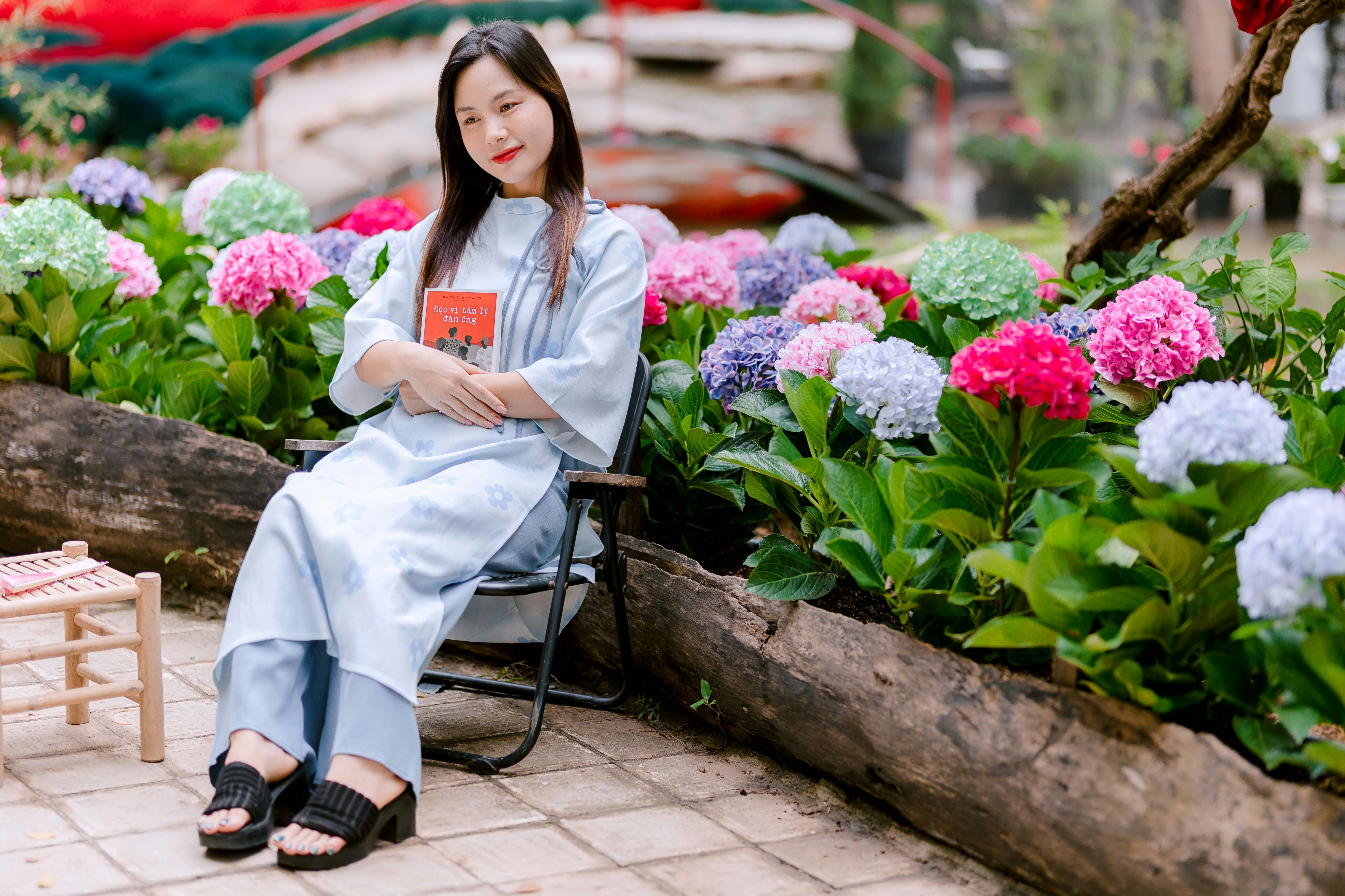 bezplatná Žena sedící v zahradě obklopená barevnými hortenziemi a držící knihu. Základová fotografie