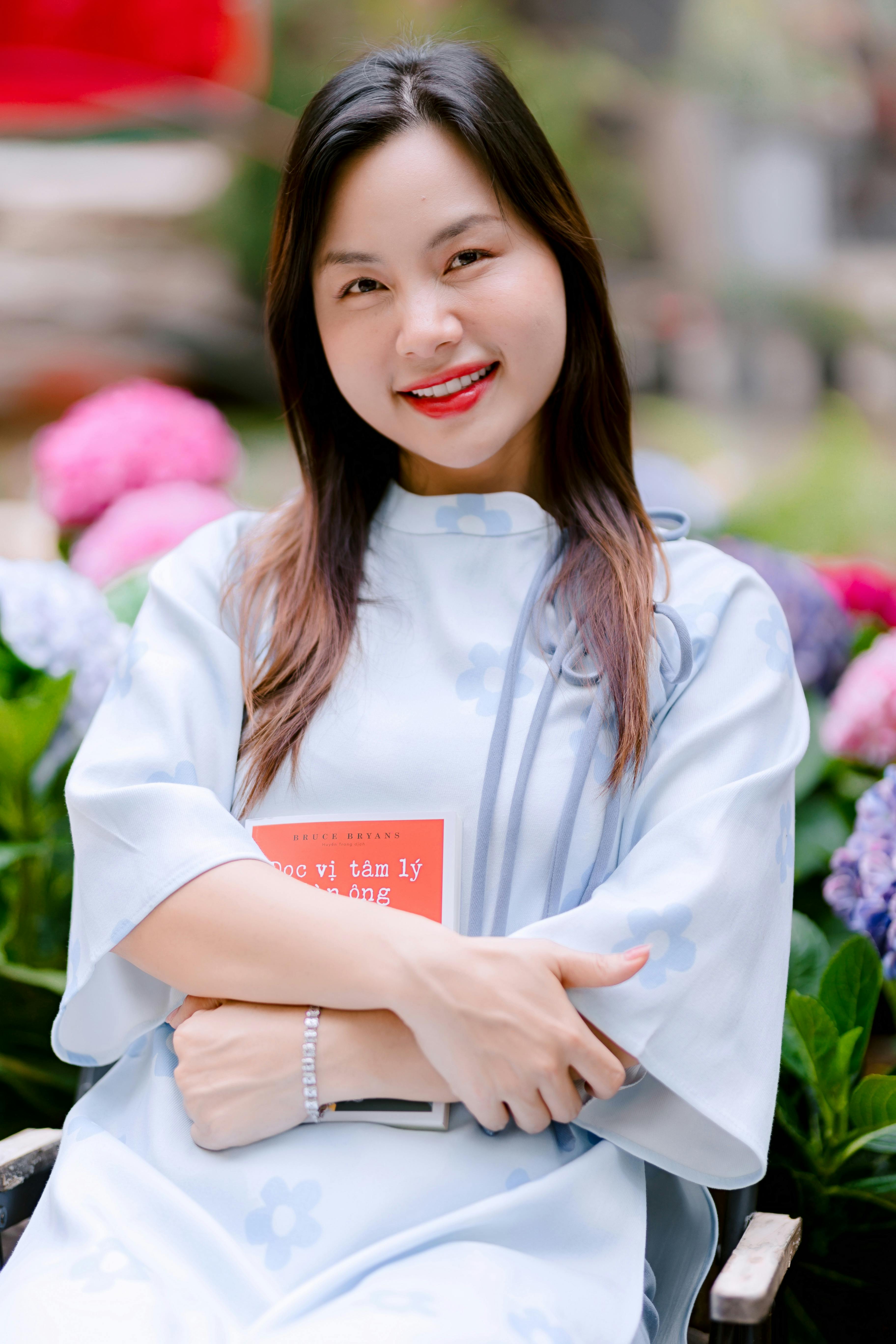 A young woman in a light blue dress smiling warmly in a garden setting.