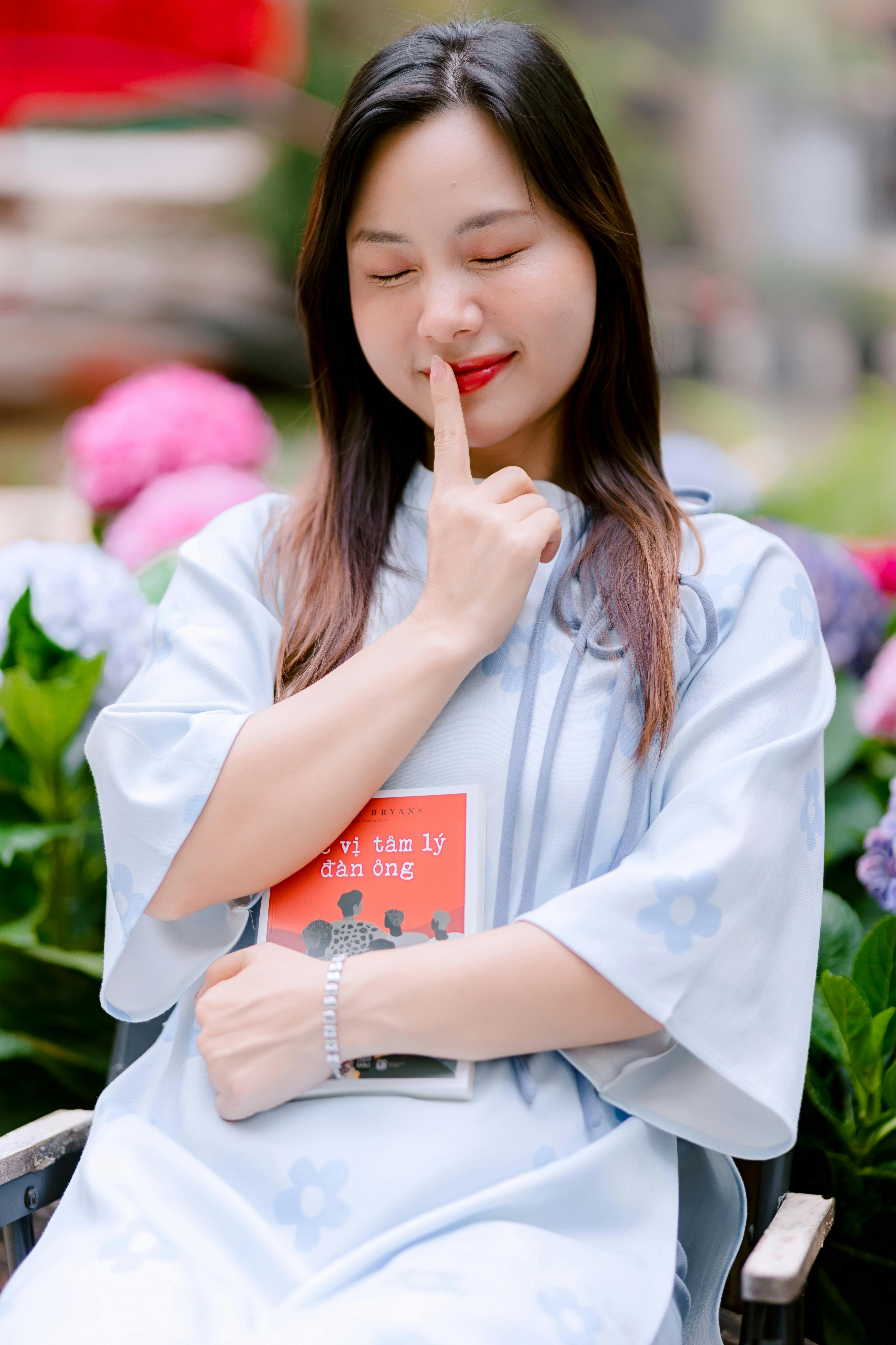 ฟรี หญิงชาวเอเชียในสวนอันเงียบสงบ กำลังถือหนังสือจิตวิทยาและครุ่นคิดอย่างลึกซึ้ง คลังภาพถ่าย