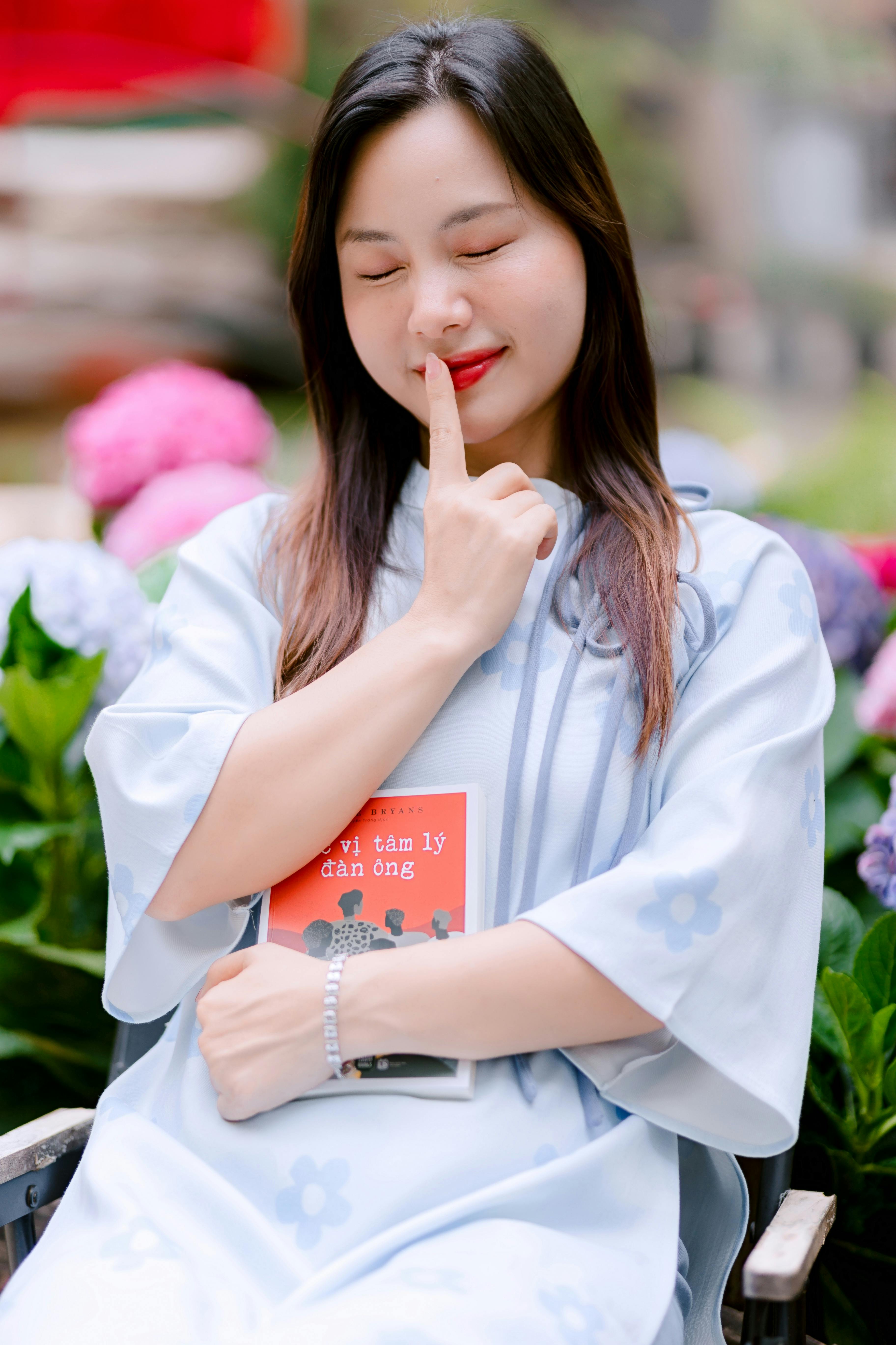 Zadarmo Šťastná žena s úsmevom drží knihu v ruke, zatiaľ čo sedí v farebnej záhrade. Fotka z fotobanky