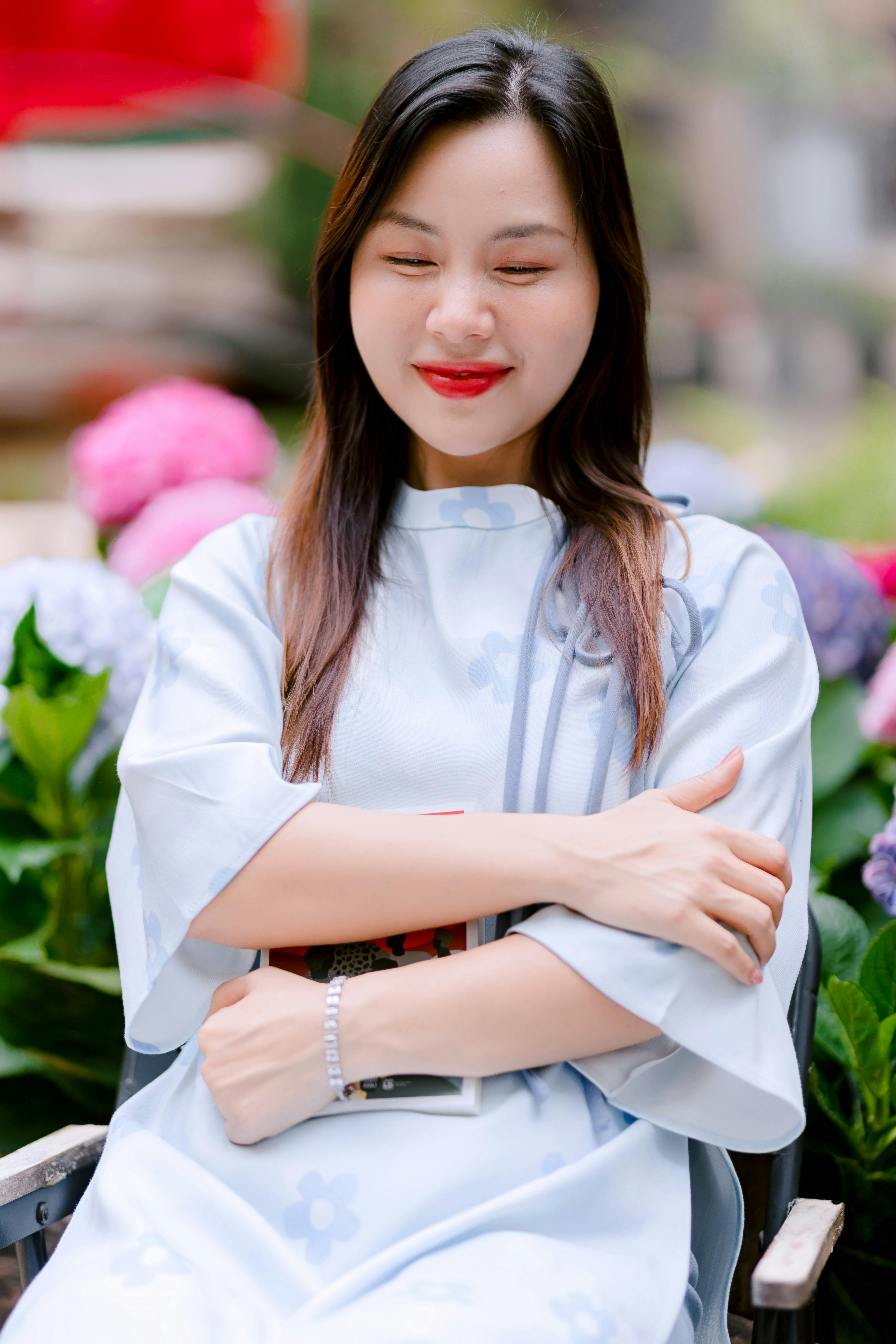 免費 一位身著傳統服飾的微笑女子，被戶外盛開的花朵環繞。 圖庫相片