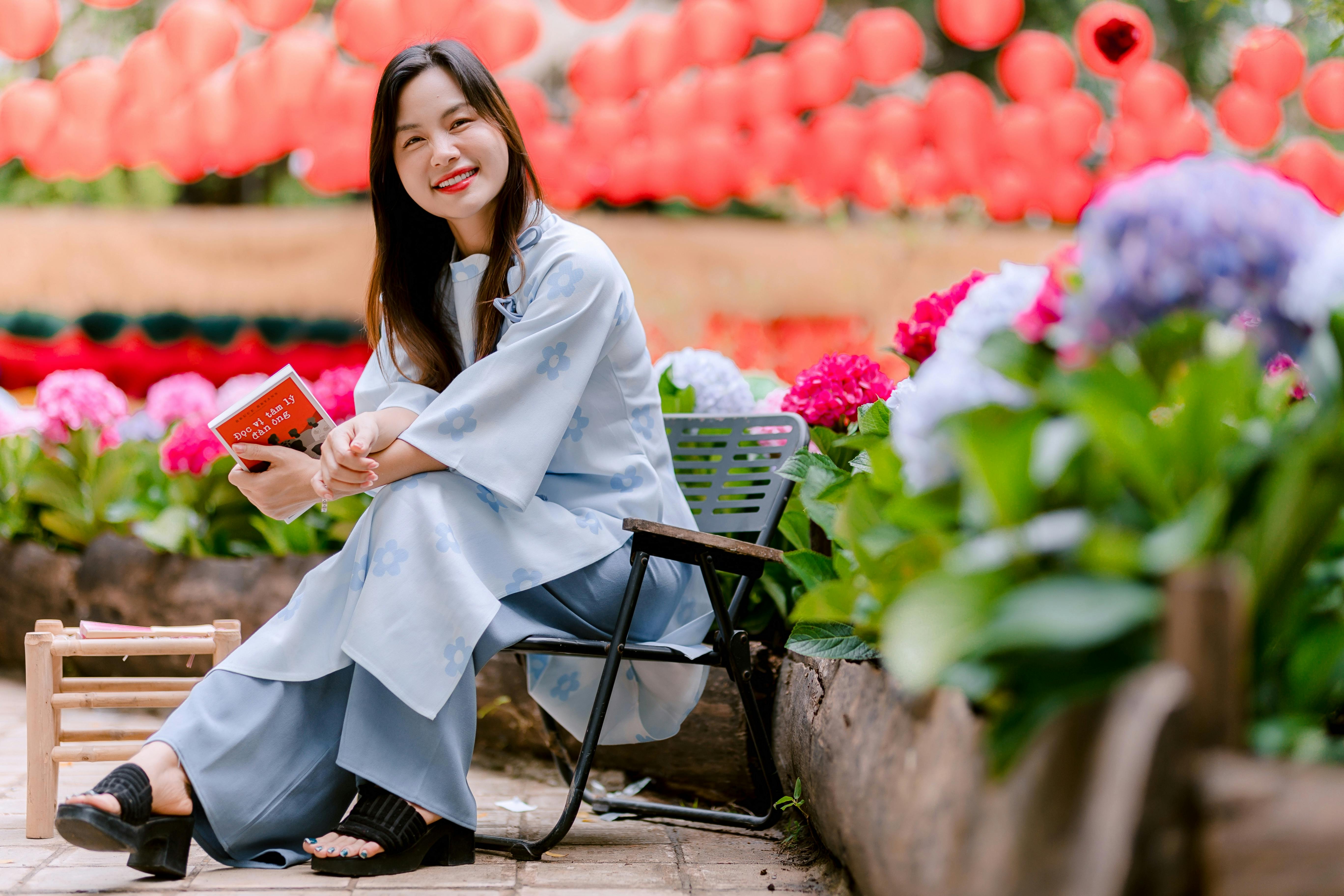 Zadarmo Žena v tradičnom odeve číta knihu medzi kvitnúcimi kvetmi s červenými lampášmi nad hlavou. Fotka z fotobanky
