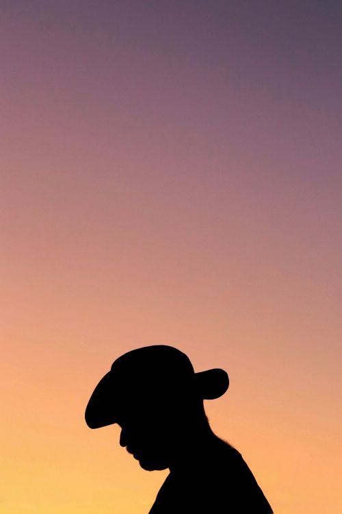 Free Silhouetted cowboy with hat against a vibrant sunset sky, conveying tranquility and solitude. Stock Photo