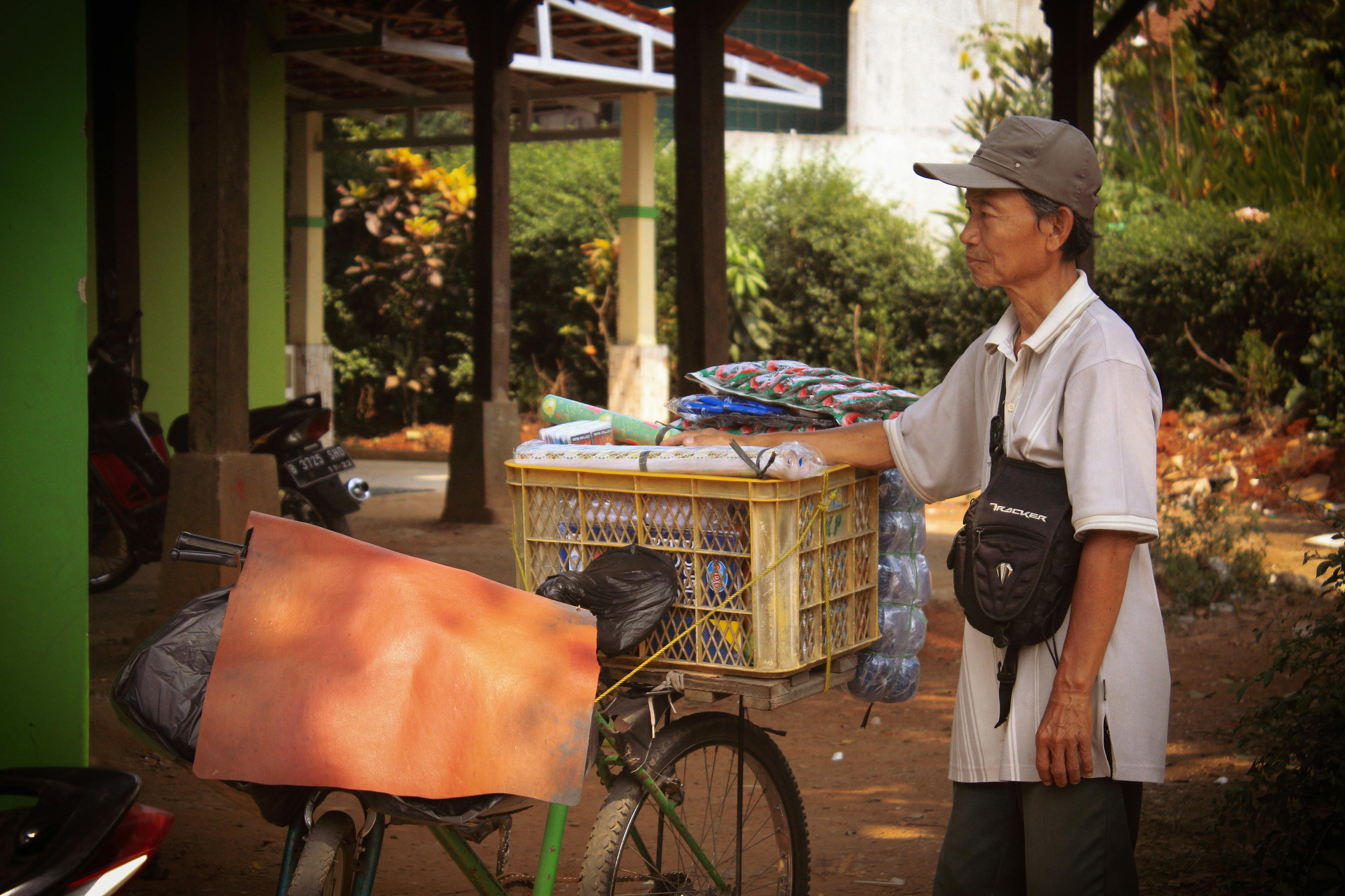 Miễn phí Một người đàn ông đứng cạnh chiếc xe đạp chất đầy hàng hóa, ngoài trời ở một khu vực râm mát. Ảnh lưu trữ