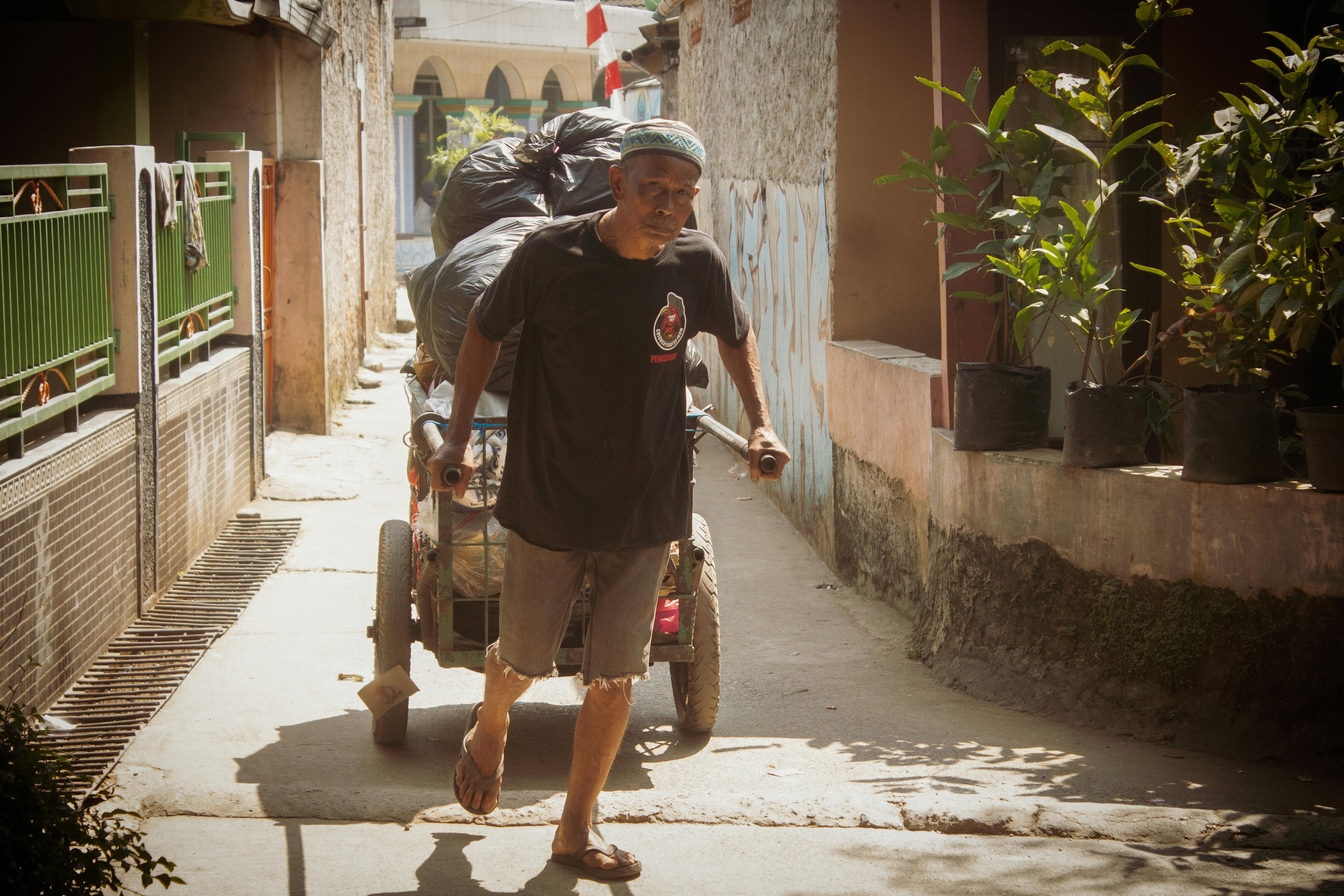 免费 一位老人拉着一辆装满袋子的手推车穿过狭窄的小巷。 素材图片