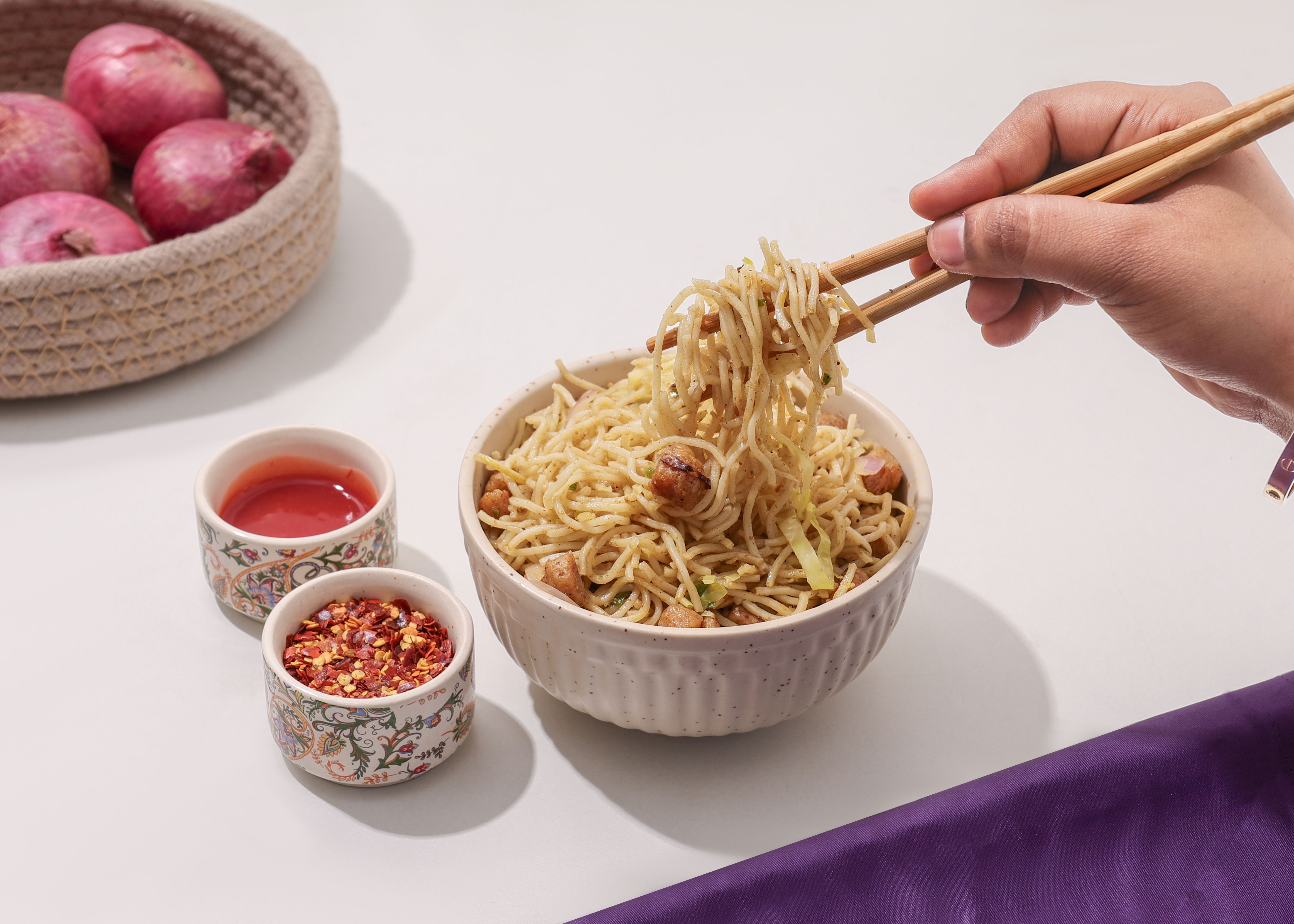 A bowl of spaghetti with chopsticks, chili flakes, and sauce, set in New Delhi, India.