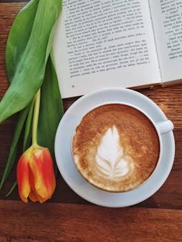 木桌上摆着卡布奇诺、书籍和郁金香，构成了一幅舒适的场景