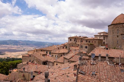 Free A stunning view of traditional Italian rooftops with a beautiful countryside backdrop under a cloud-filled sky. Stock Photo