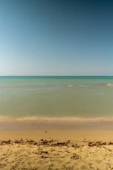 Serene beach scene on Italy's coast capturing tranquil azure waters and sandy shores under clear summer skies.