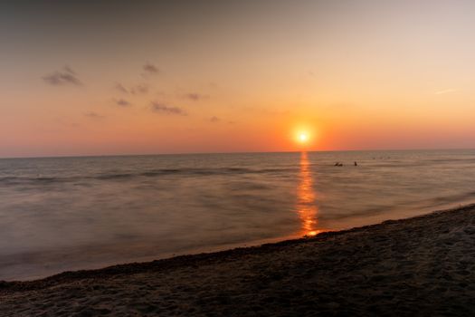 Peaceful sunset over an Italian beach with golden hues reflecting on the calm sea.