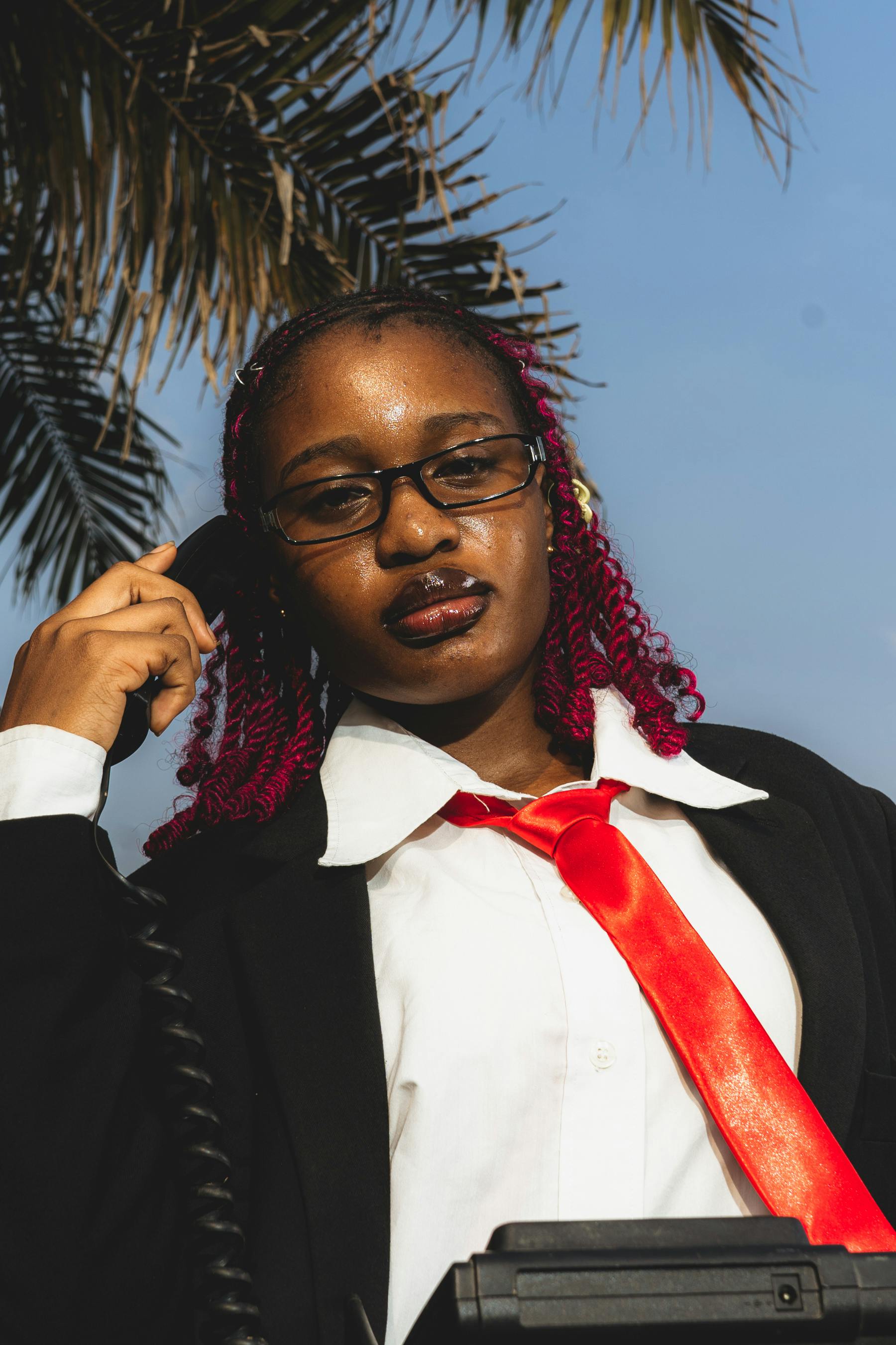 ฟรี หญิงสาวมั่นใจในชุดทำงานกำลังคุยโทรศัพท์อยู่ใต้ต้นปาล์มที่แสงแดดส่องถึง คลังภาพถ่าย