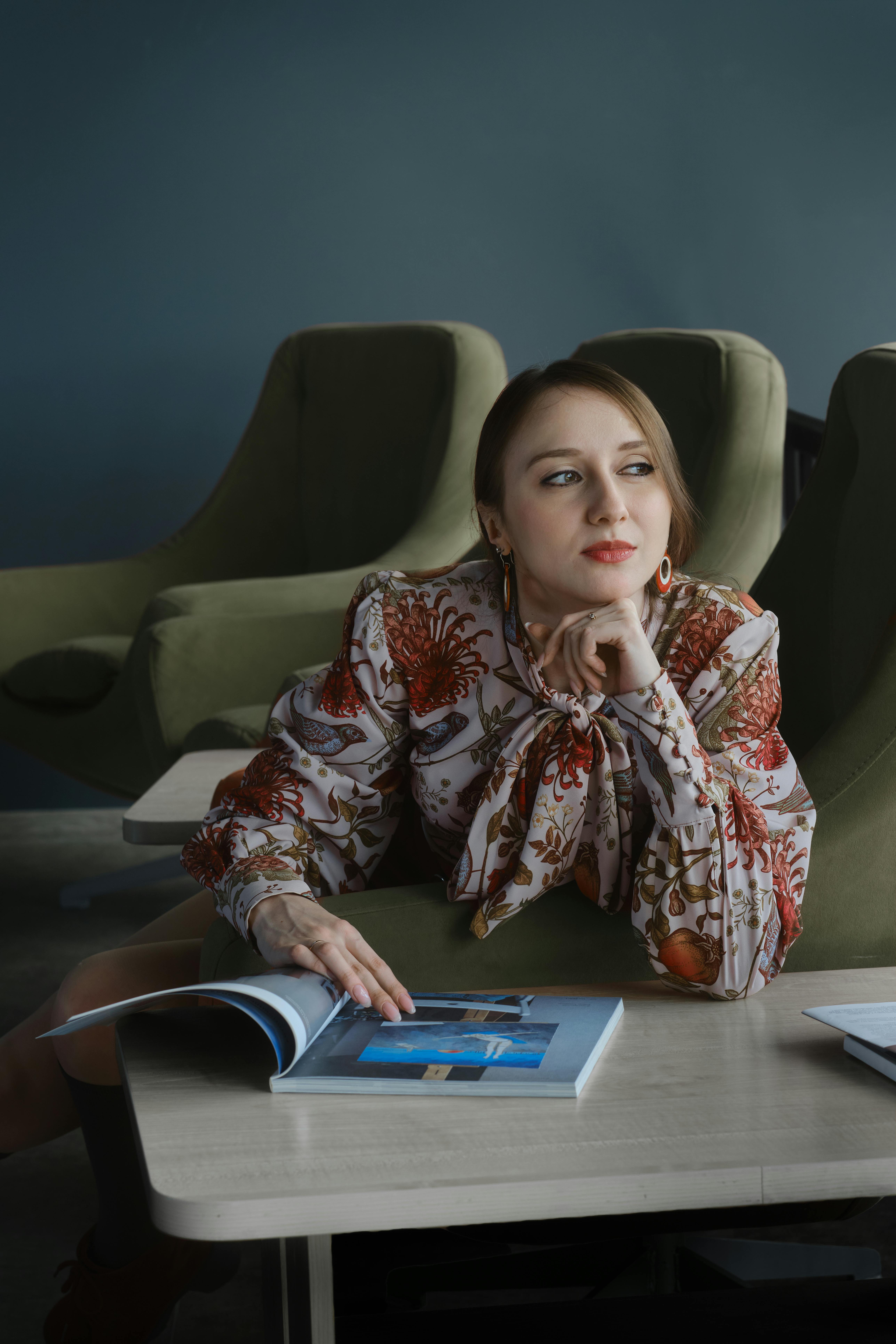 Miễn phí Một người phụ nữ trầm tư trong chiếc áo sơ mi hoa thanh lịch đang đọc tạp chí trong nhà, ngồi trên một chiếc ghế hiện đại. Ảnh lưu trữ