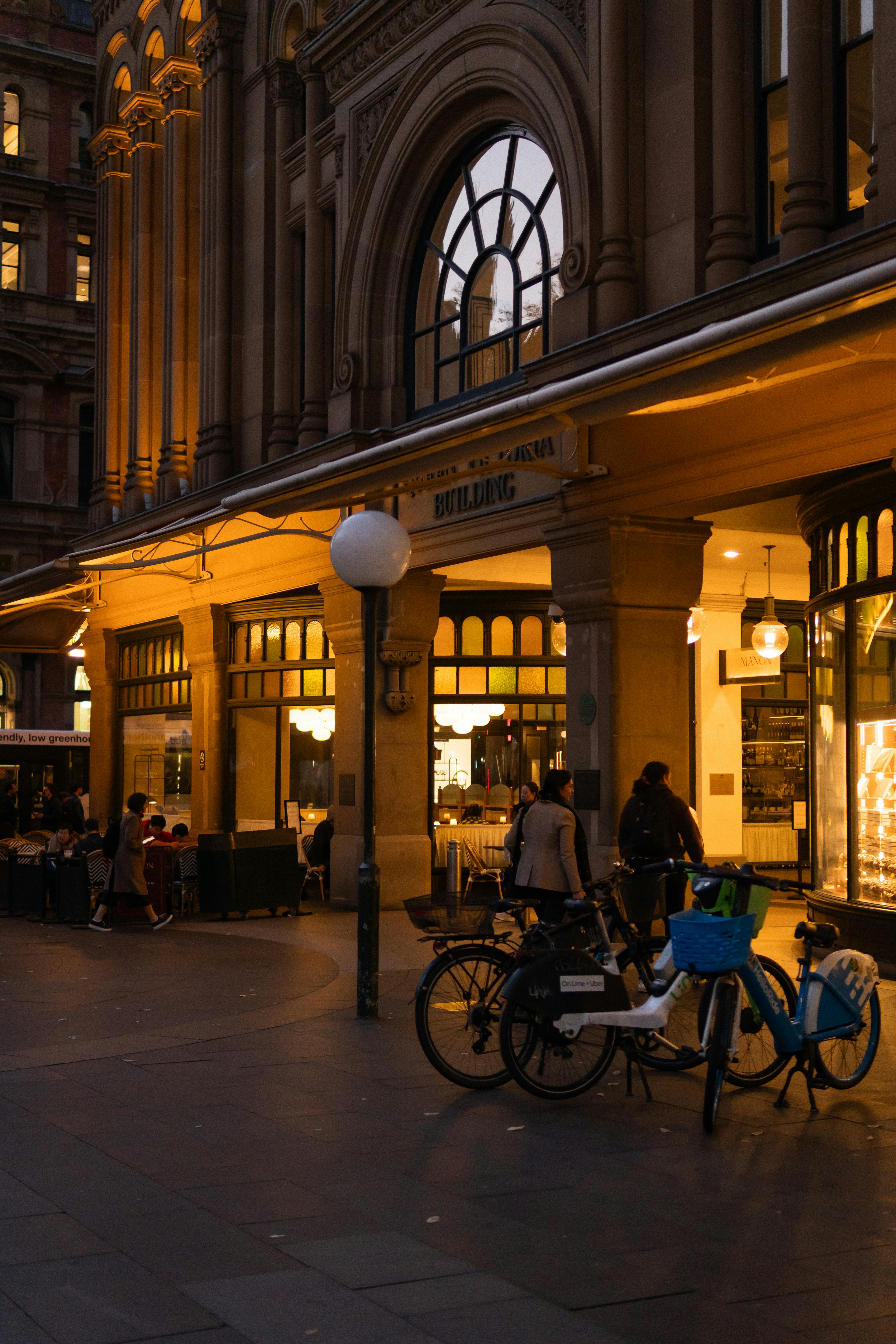 免費 人們在歷史悠久的城市建築外享受夜晚的時光，溫暖的燈光和附近停放的自行車營造出宜人的氛圍。 圖庫相片