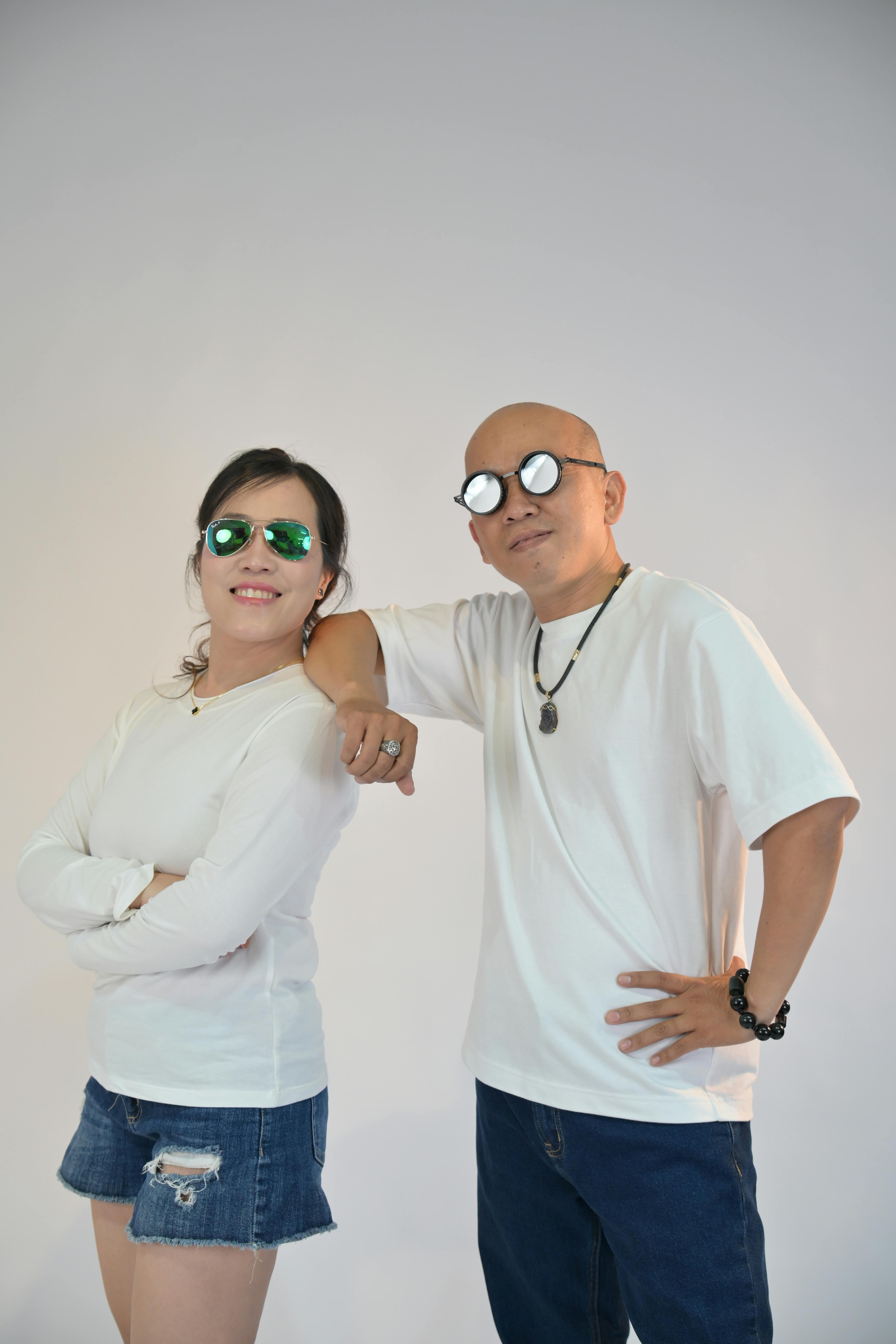 Безкоштовне Стильна пара в сонцезахисних окулярах і білих топах позує в студійній обстановці. стокове фото