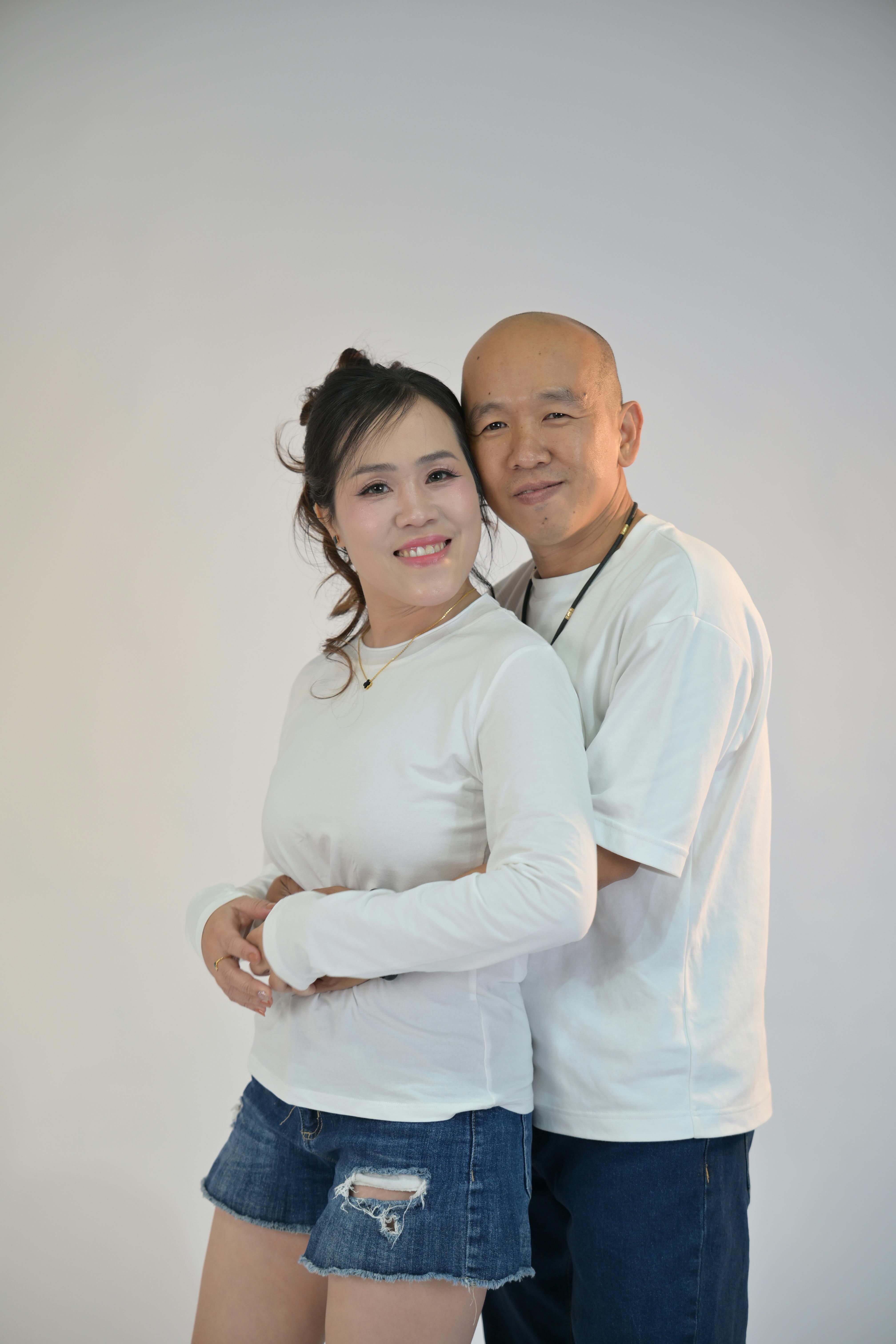 bezplatná Usmívající se pár v bílých košilích láskyplně pózuje na prostém pozadí. Základová fotografie