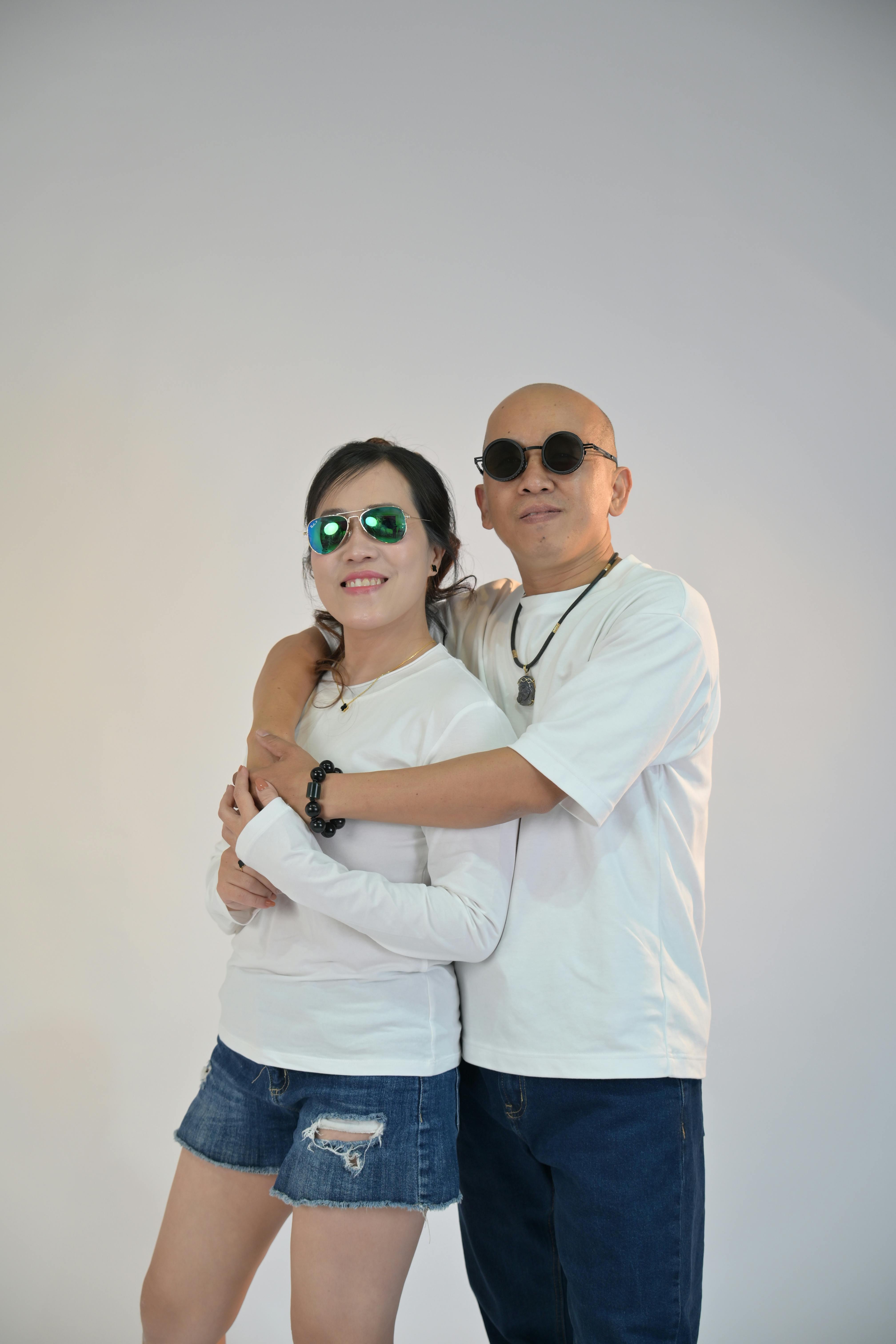 bezplatná Šťastný pár v slunečních brýlích pózuje ležérně ve studiu s bílým pozadím. Základová fotografie