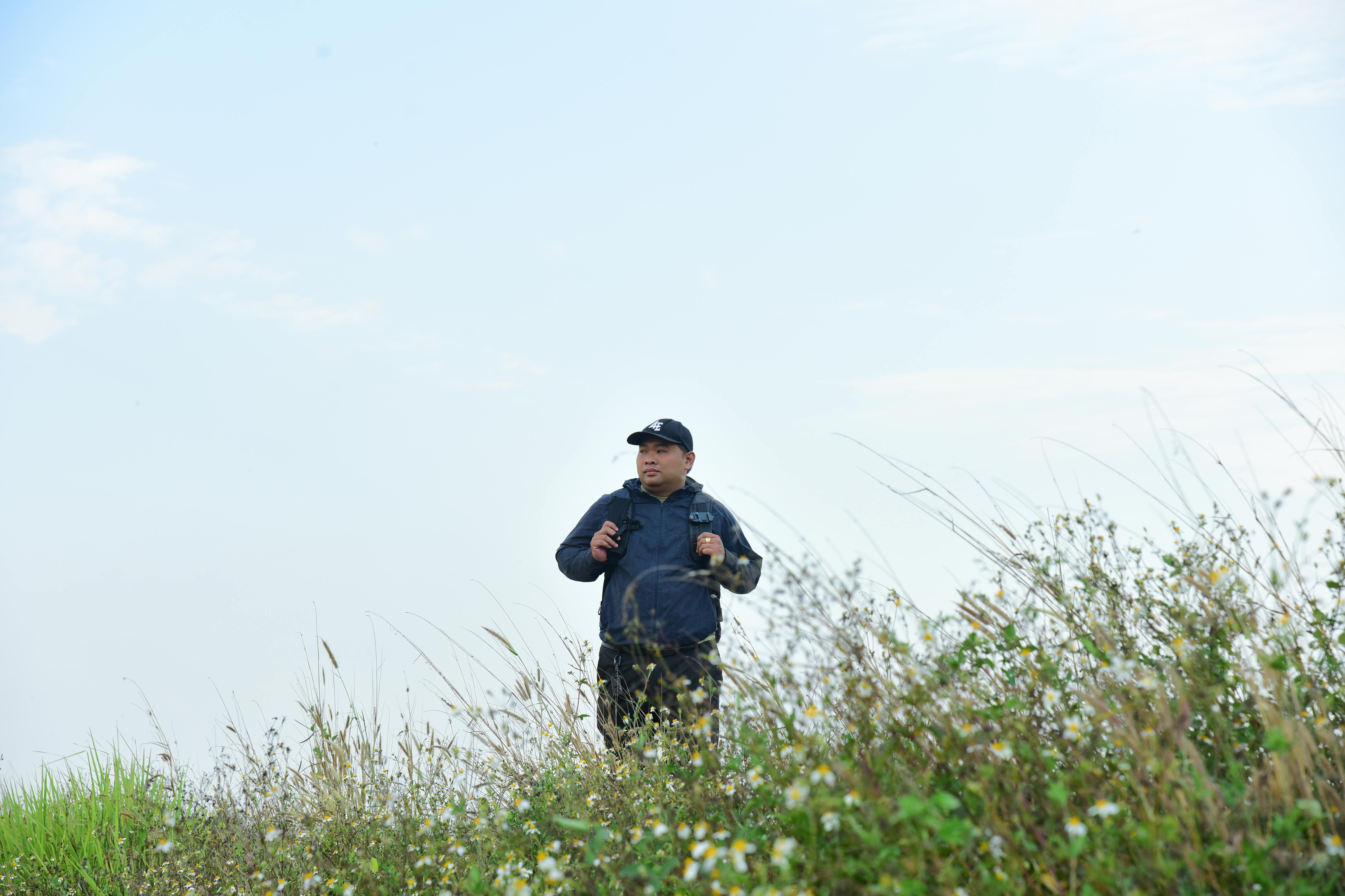 무료 푸른 하늘 아래 키 큰 풀숲 사이에서 기기를 들고 있는 사람. 스톡 사진