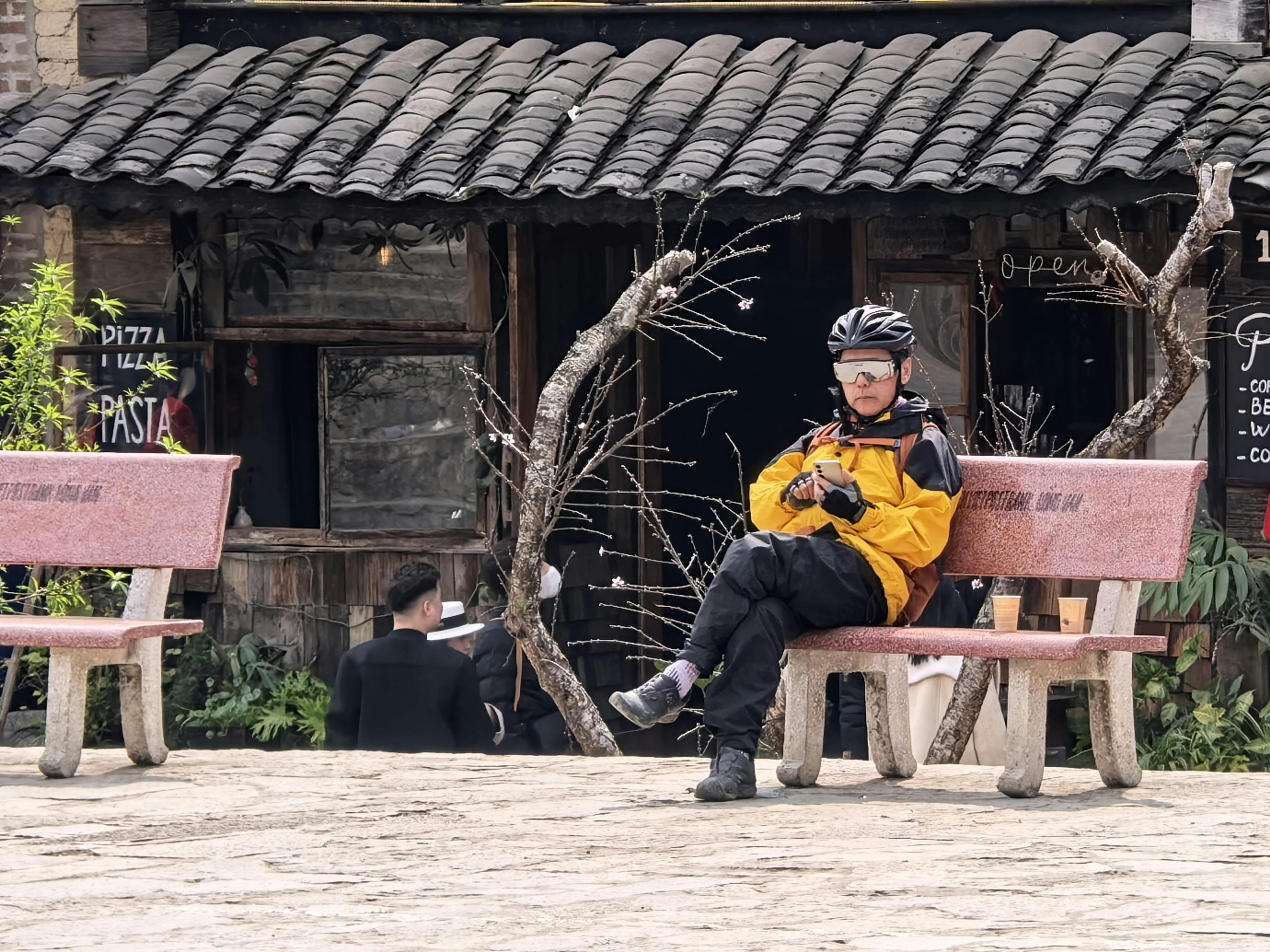 ฟรี นักปั่นจักรยานในชุดสีสดใส นั่งอยู่บนม้านั่งด้านนอกร้านกาแฟสไตล์ชนบท เพลิดเพลินกับการพักผ่อนอย่างสงบสุข คลังภาพถ่าย