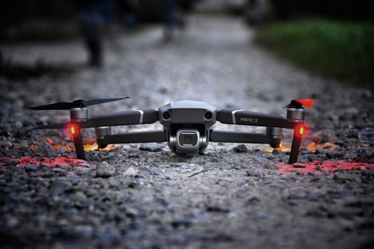 A modern drone with glowing lights sits on a gravel path at twilight, ready for flight.