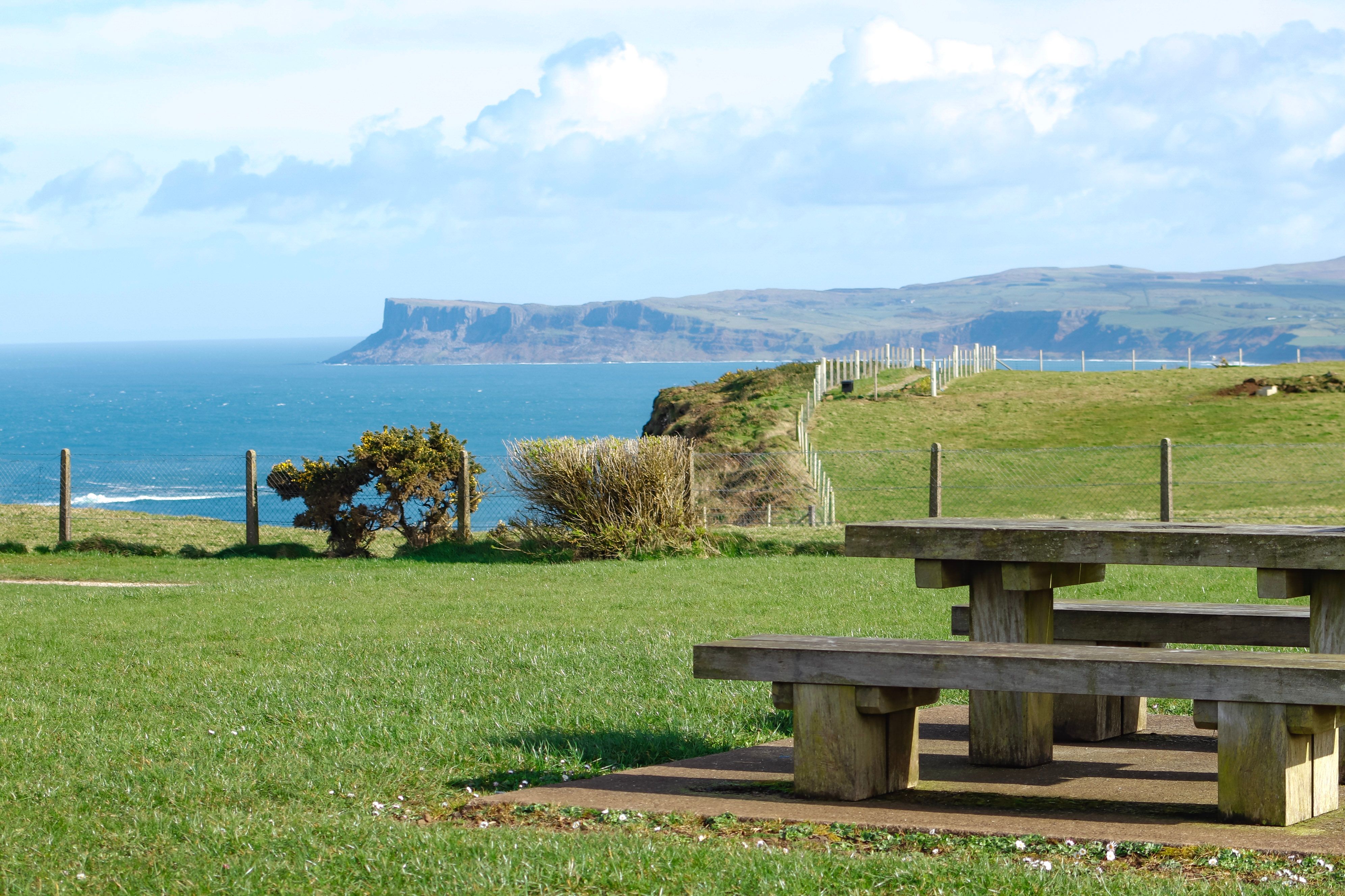 Scenic coastal landscape with cliffs, sea, and a wooden picnic table.