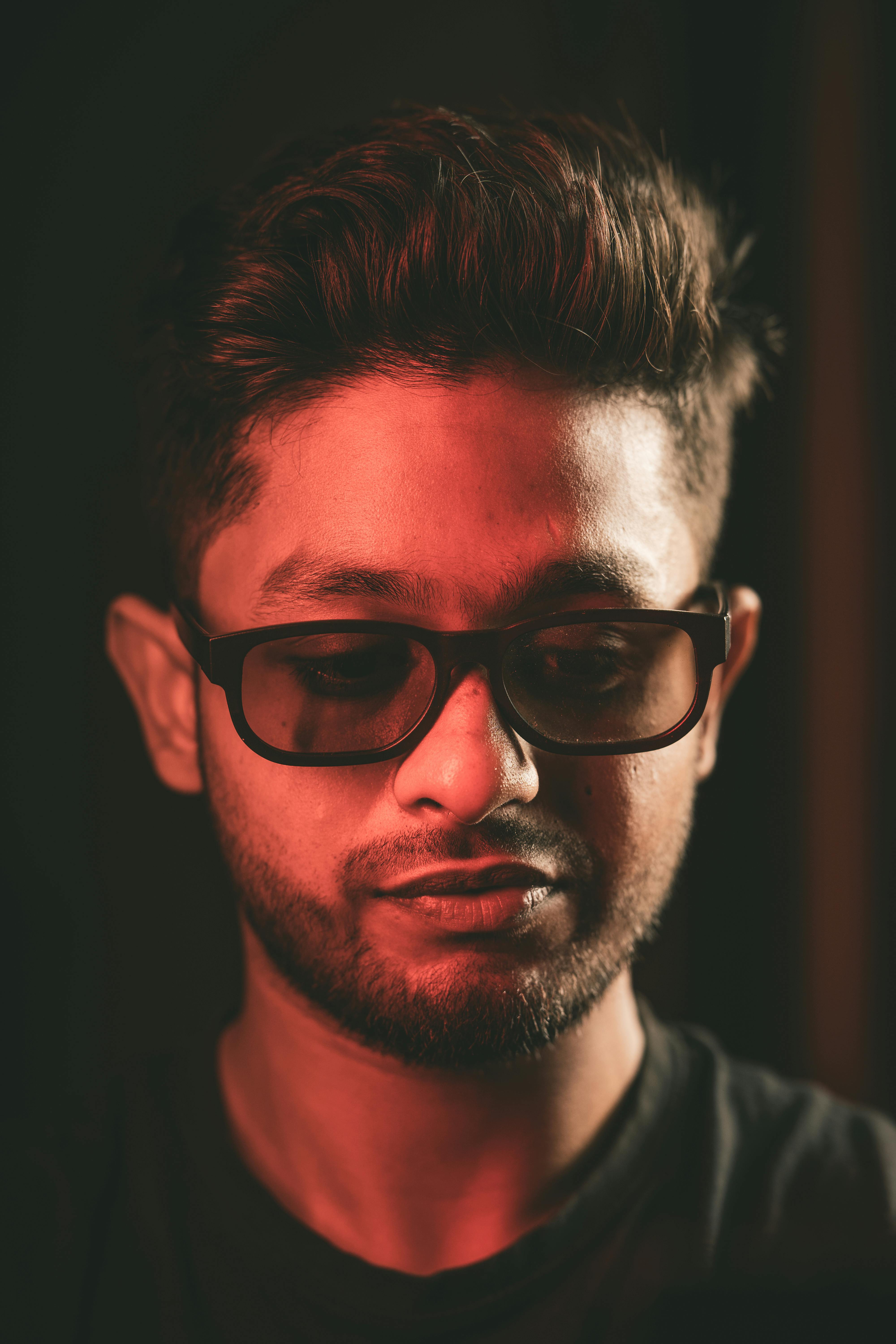 Безкоштовне Крупний план портрета дорослого чоловіка в сонцезахисних окулярах, освітленого червоним світлом, що створює драматичний ефект. стокове фото