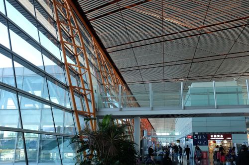 Free Wide-angle view of a bustling airport terminal featuring modern geometric architecture and natural lighting. Stock Photo
