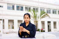 一名年轻女子身穿蓝色外套，在城市建筑的背景下于户外使用手机