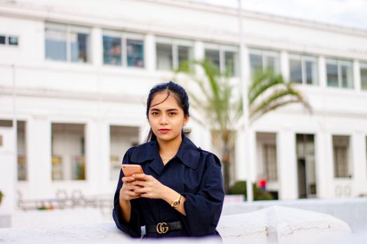 一名年轻女子身穿蓝色外套，在城市建筑的背景下于户外使用手机