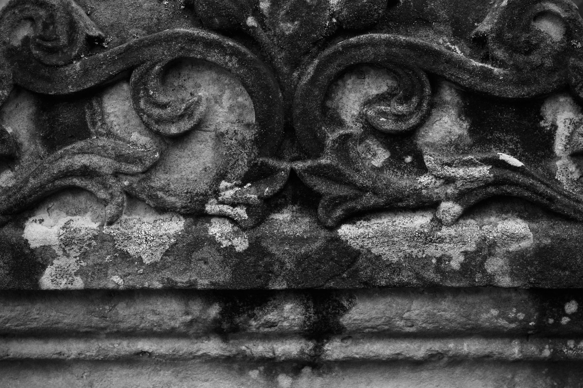 Black and white image of decorative stone carving showcasing worn textures and intricate patterns.
